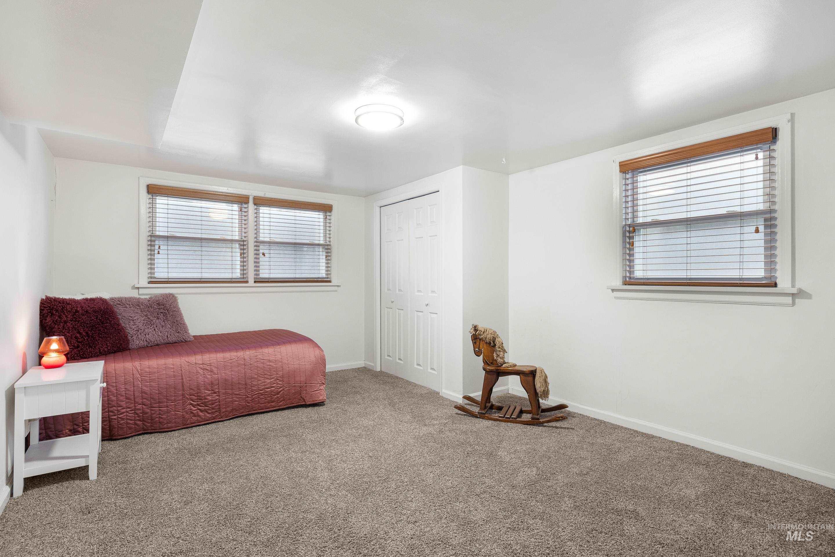 Carpeted bedroom with multiple windows and a closet