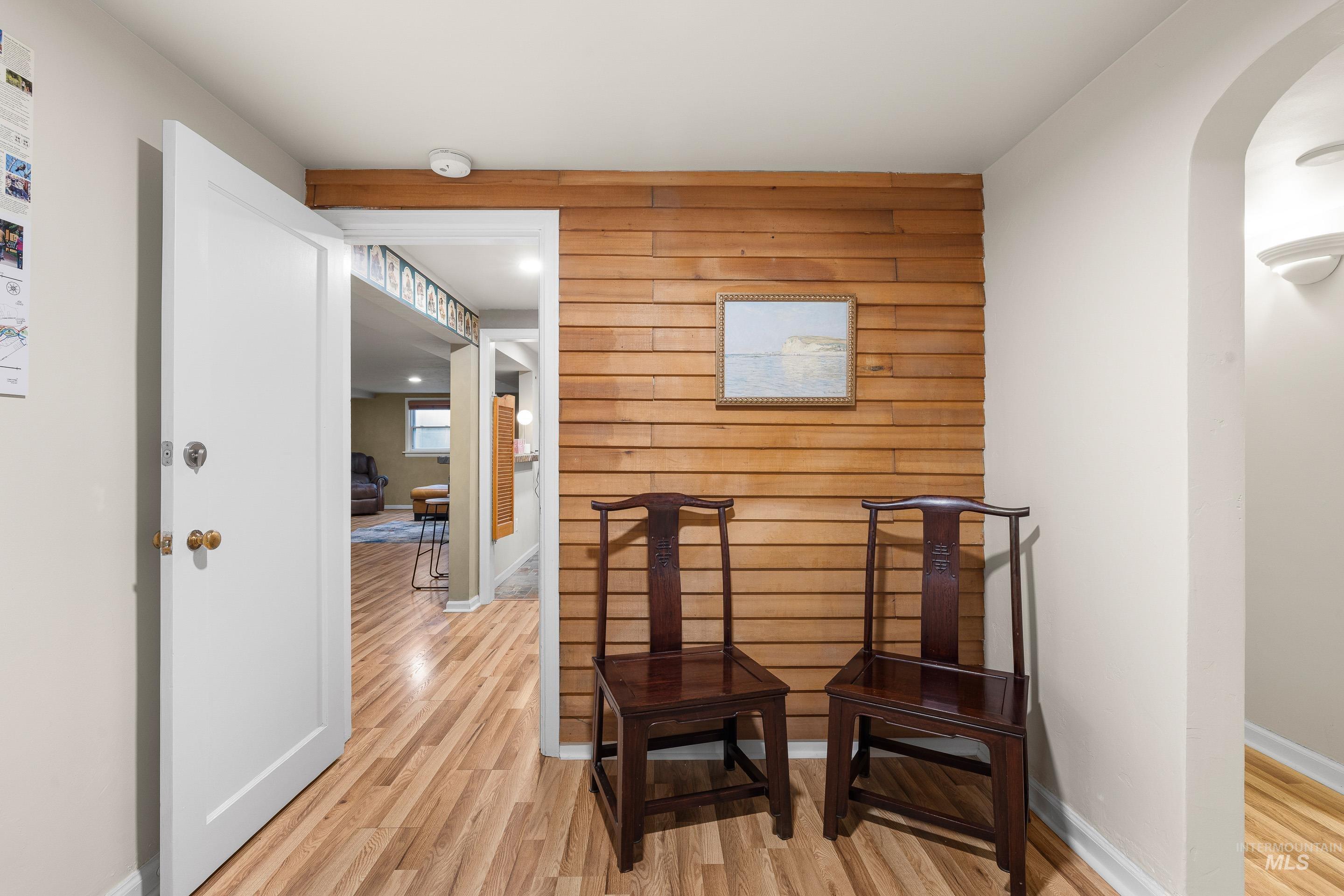 Living area with an accent wall, light wood-style flooring, wooden walls, and arched walkways