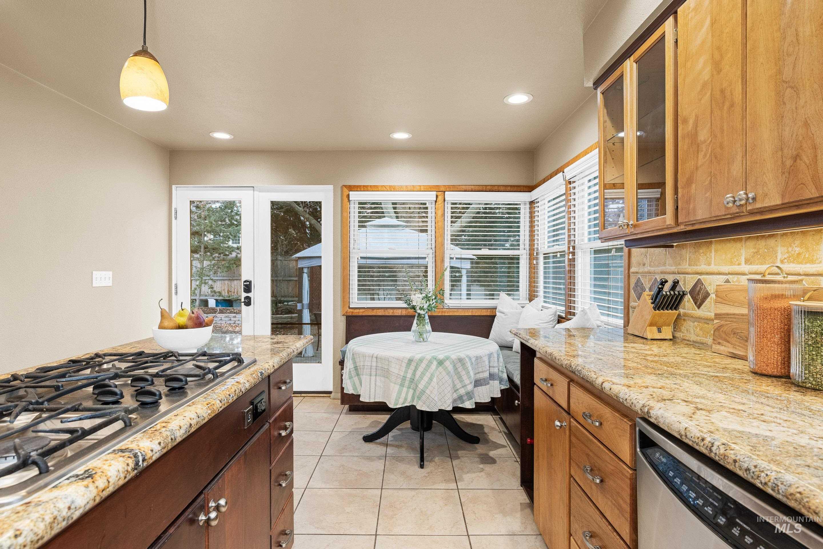 Kitchen featuring decorative light fixtures, light stone countertops, glass insert cabinets, stainless steel appliances, and light tile patterned floors