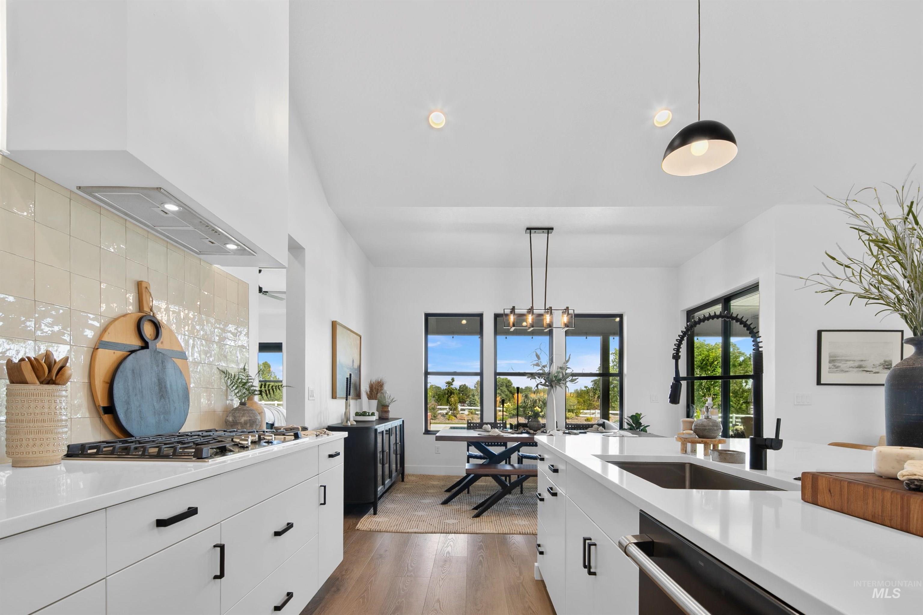 Kitchen with white cabinets, hanging light fixtures, light wood finished floors, appliances with stainless steel finishes, and light stone counters
