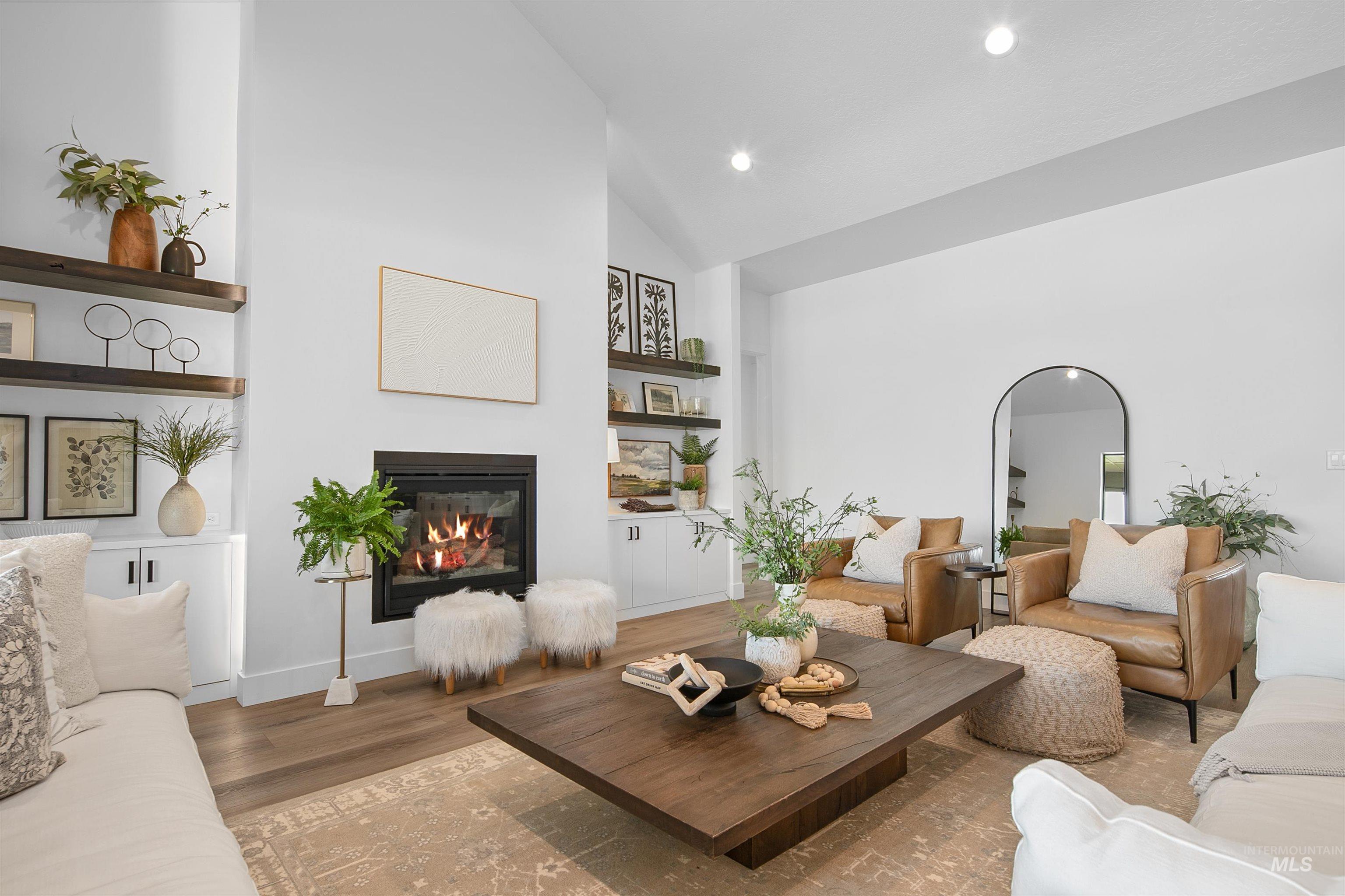 Living area featuring wood finished floors, high vaulted ceiling, a glass covered fireplace, built in shelves, and recessed lighting