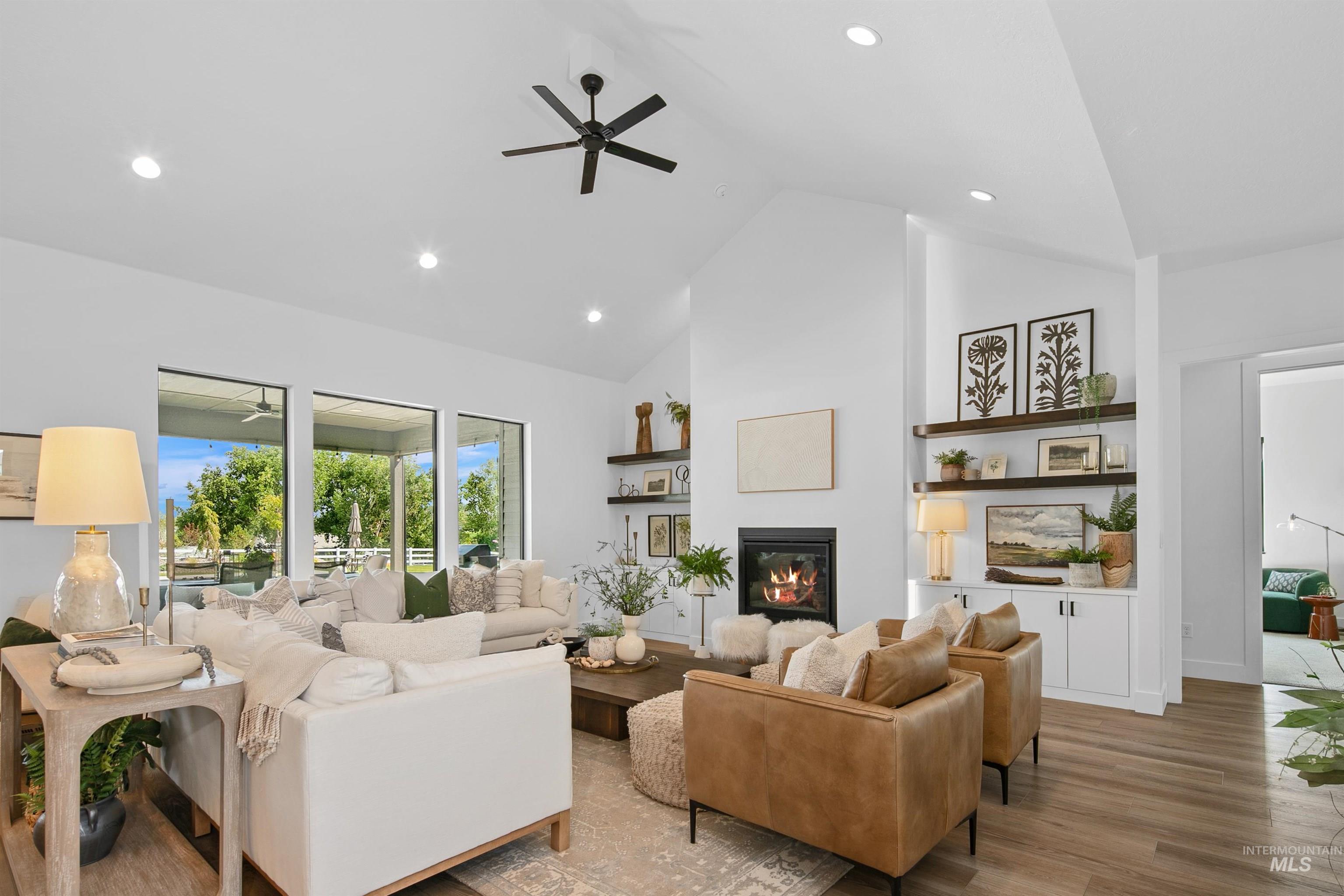 Living area featuring high vaulted ceiling, light wood-type flooring, a ceiling fan, a glass covered fireplace, and recessed lighting