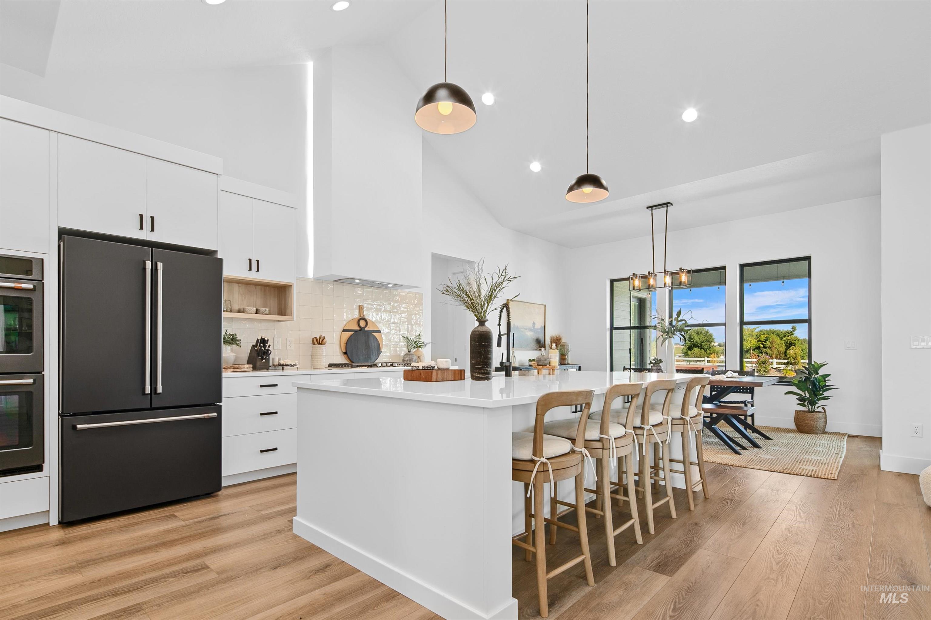 Kitchen featuring high end black refrigerator, high vaulted ceiling, hanging light fixtures, white cabinets, and light wood-style flooring