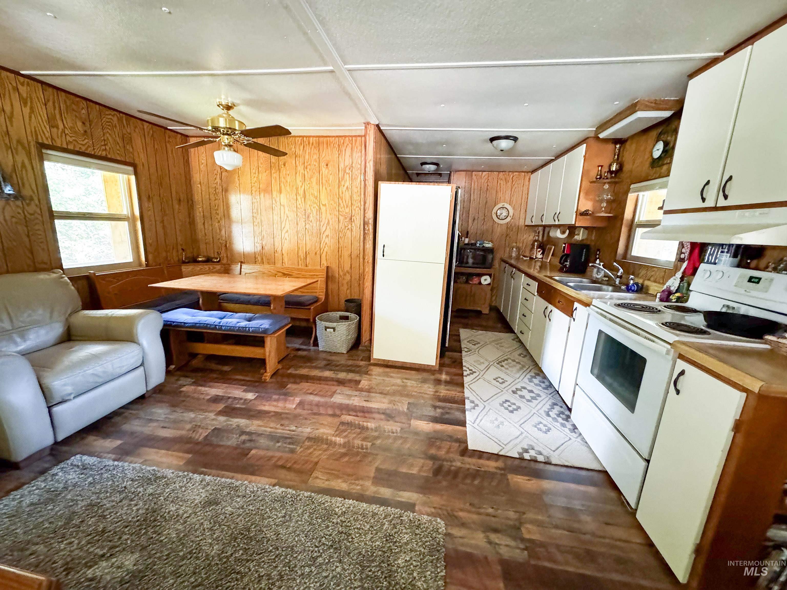 Kitchen featuring electric stove, wooden walls, light countertops, under cabinet range hood, and dark wood-style floors