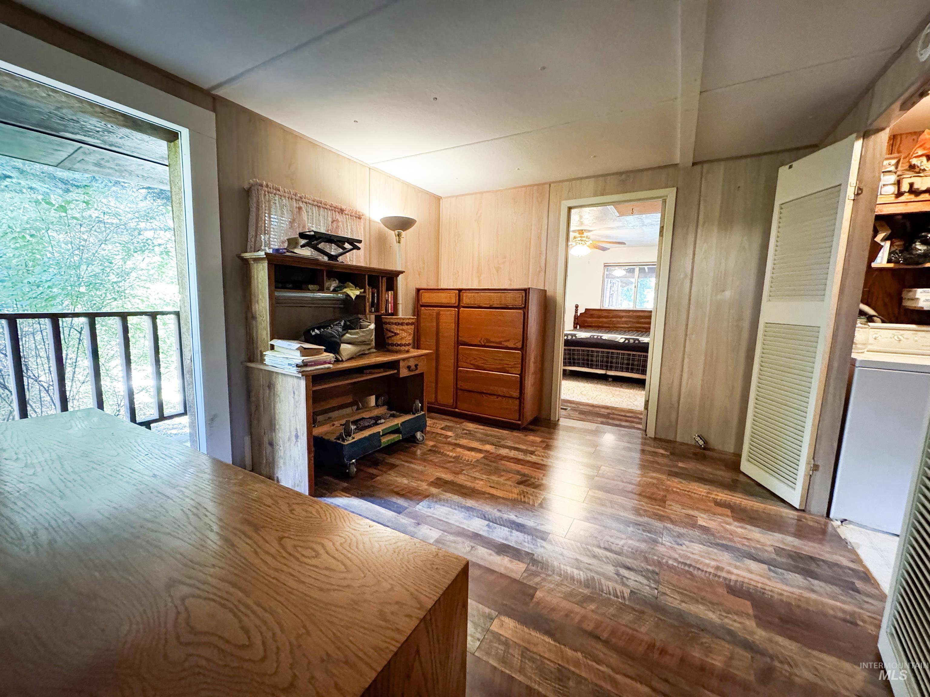Office with dark wood finished floors, wood walls, washer / clothes dryer, and a ceiling fan