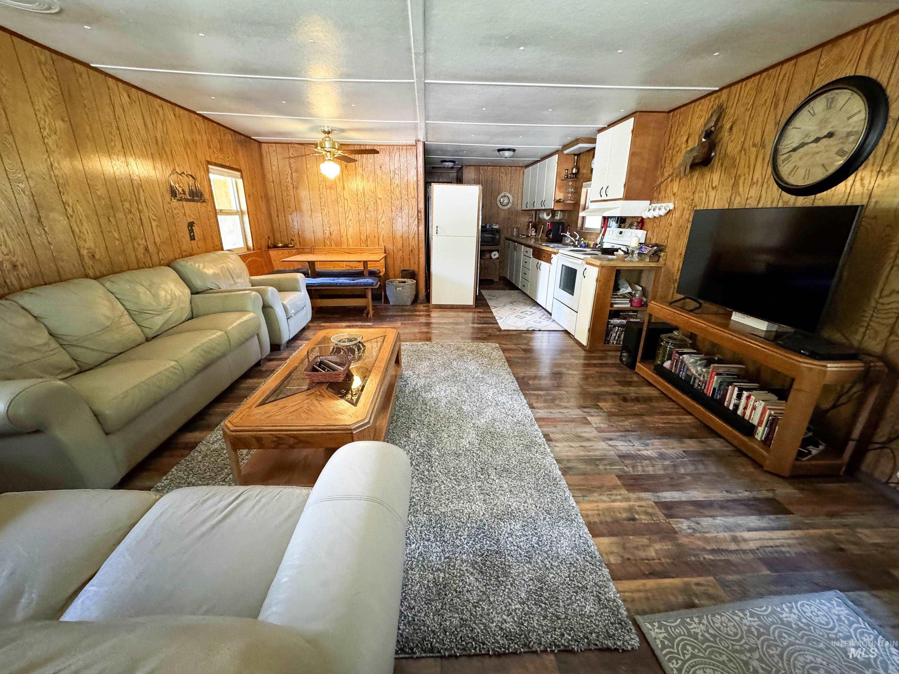 Living area with wooden walls, dark wood-style flooring, and a ceiling fan