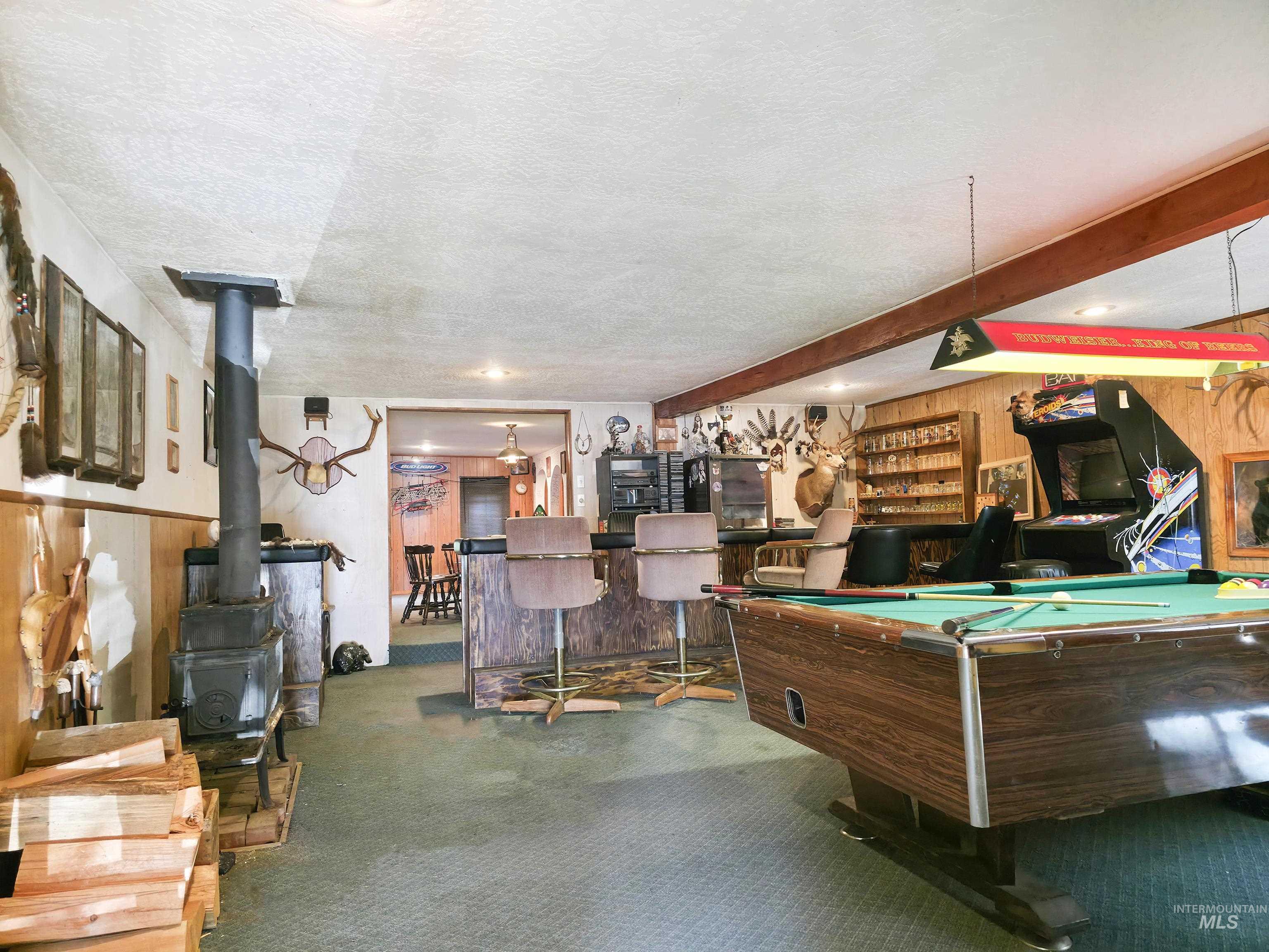 Recreation room featuring a wood stove, wood walls, billiards table, carpet, and bar