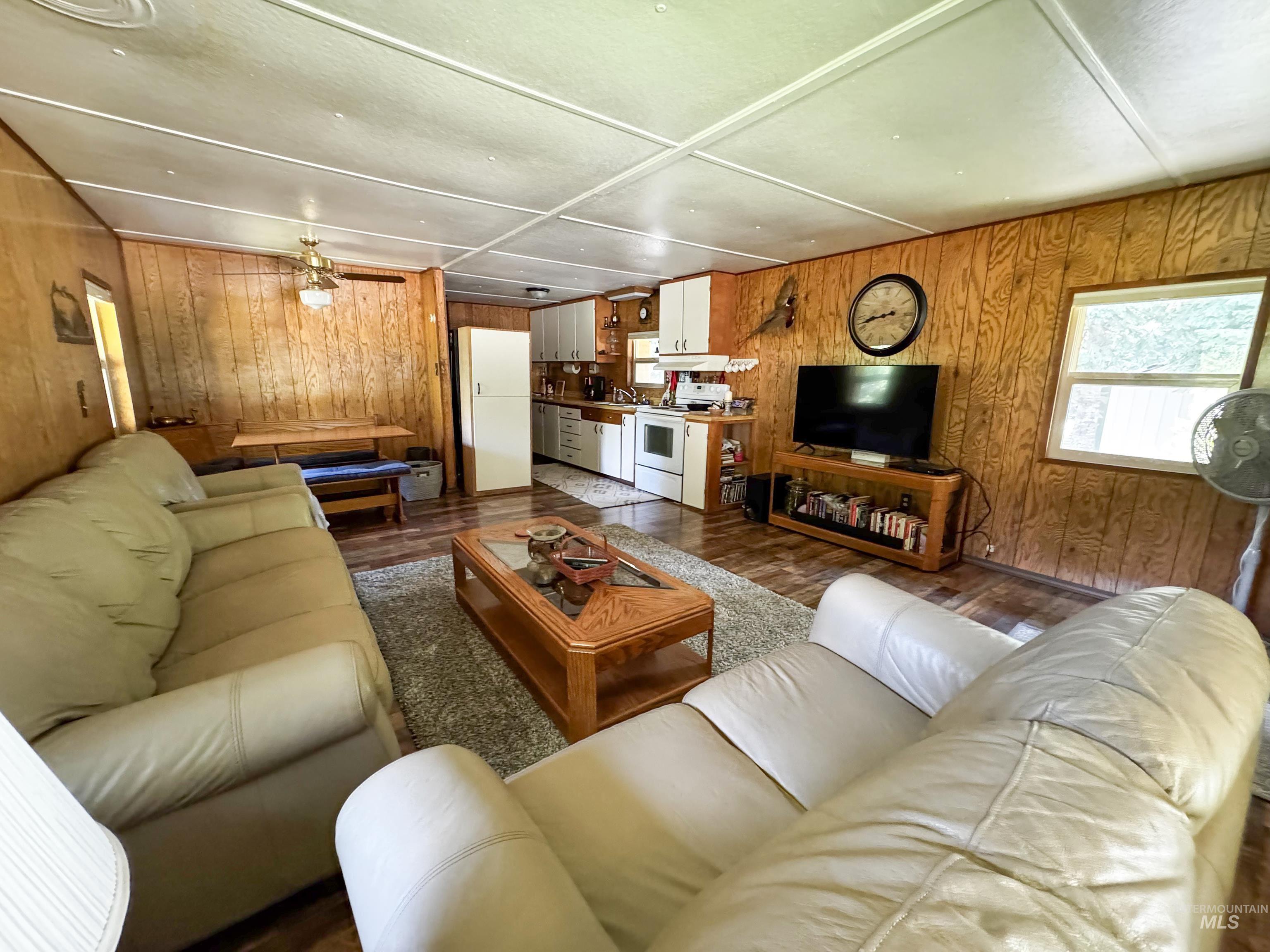 Living area with wooden walls, wood finished floors, and a ceiling fan