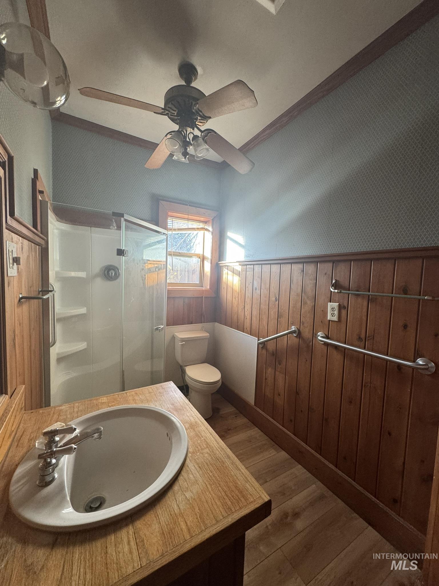 Full bath with a wainscoted wall, wood finished floors, wood walls, a shower stall, and ceiling fan