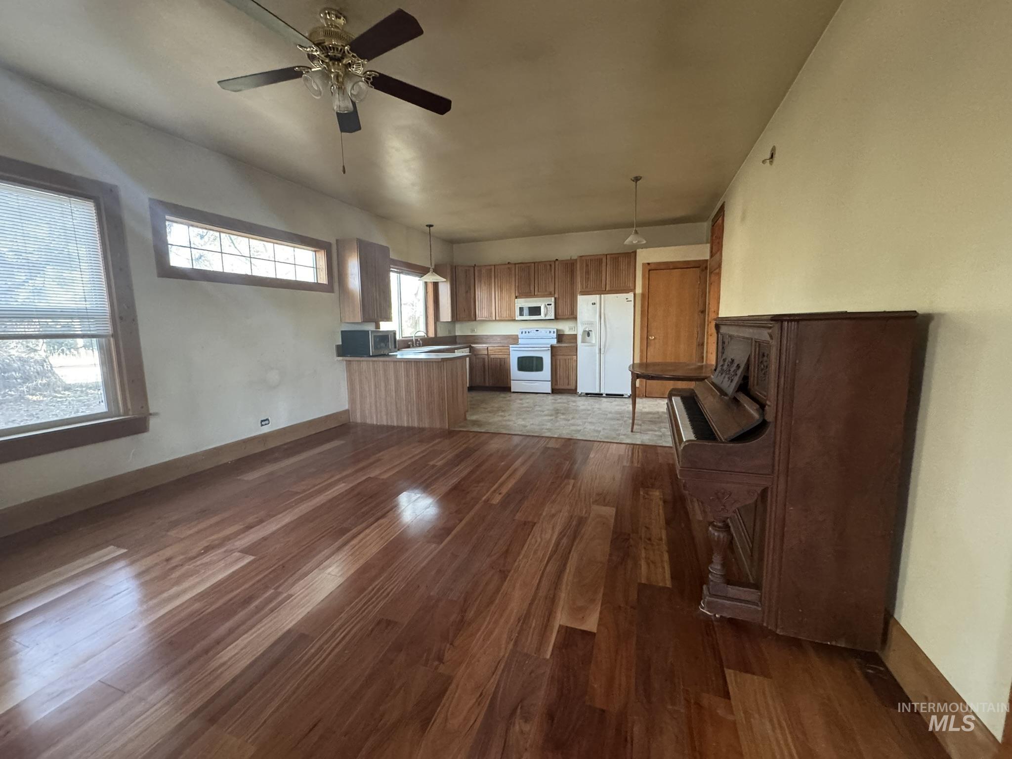 Kitchen with decorative light fixtures, brown cabinets, white appliances, ceiling fan, and dark wood-style flooring
