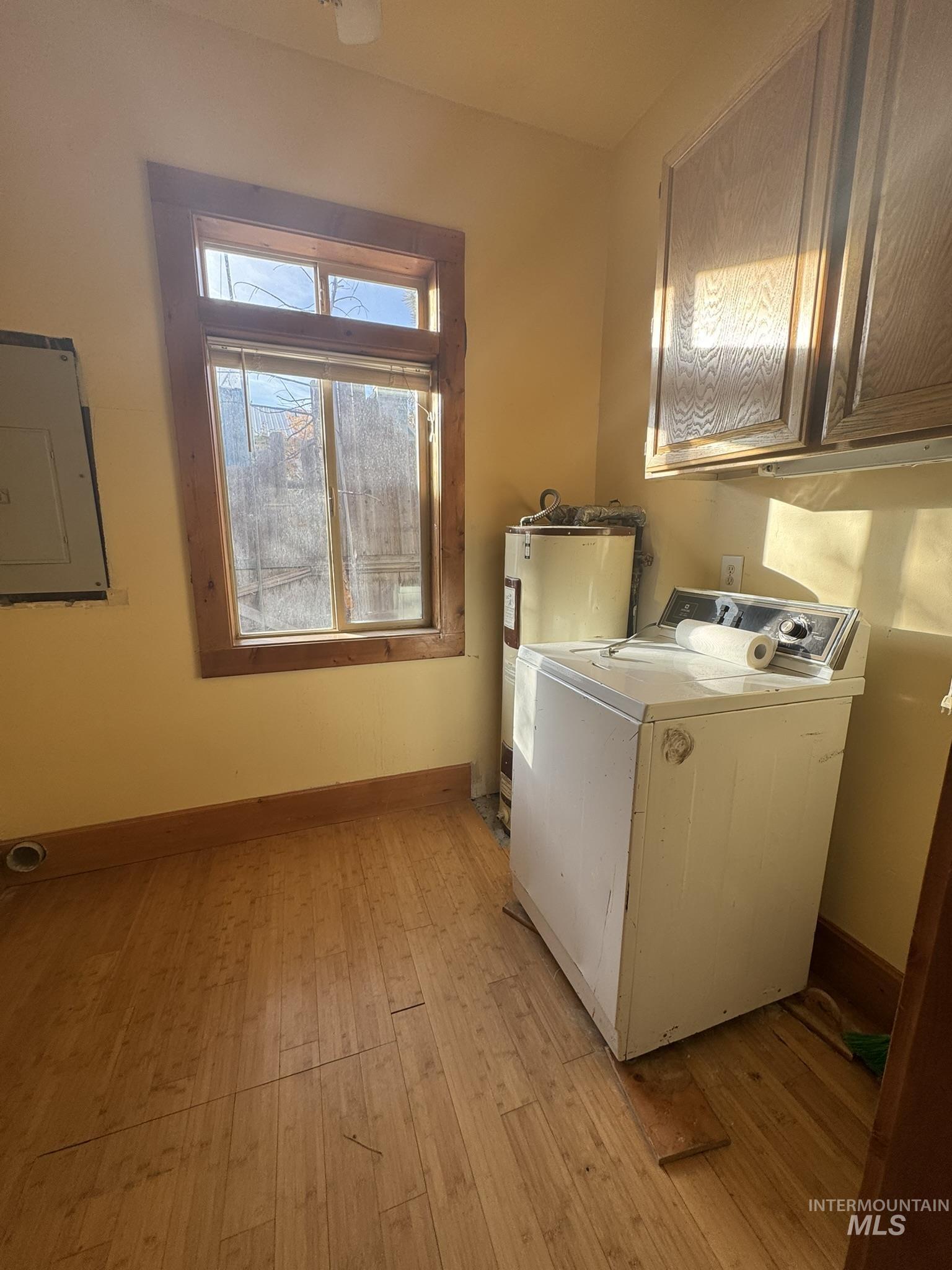 Laundry area with washer / dryer, light wood-style flooring, electric panel, cabinet space, and water heater