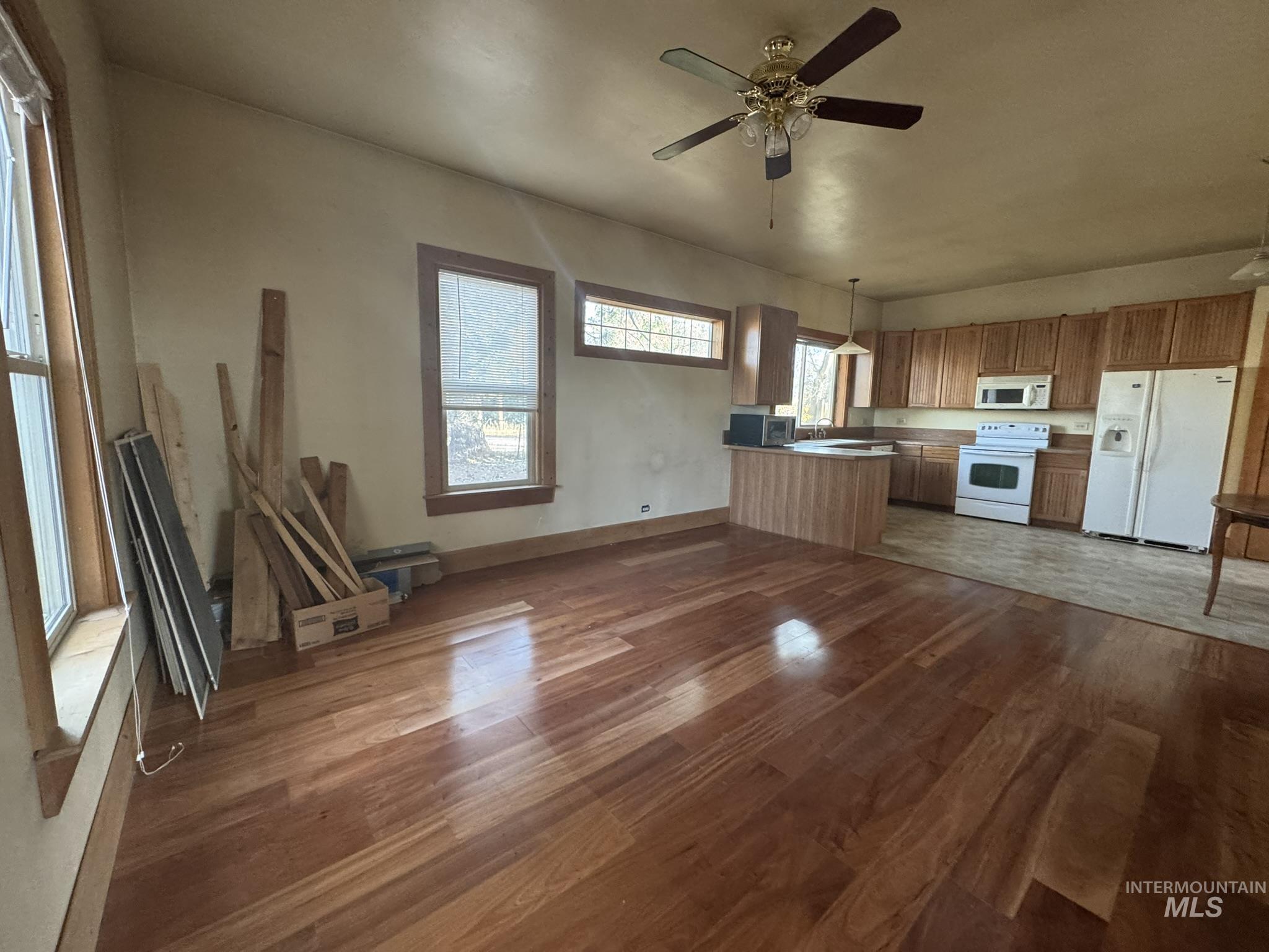 Kitchen featuring white appliances, decorative light fixtures, dark wood-type flooring, open floor plan, and a peninsula
