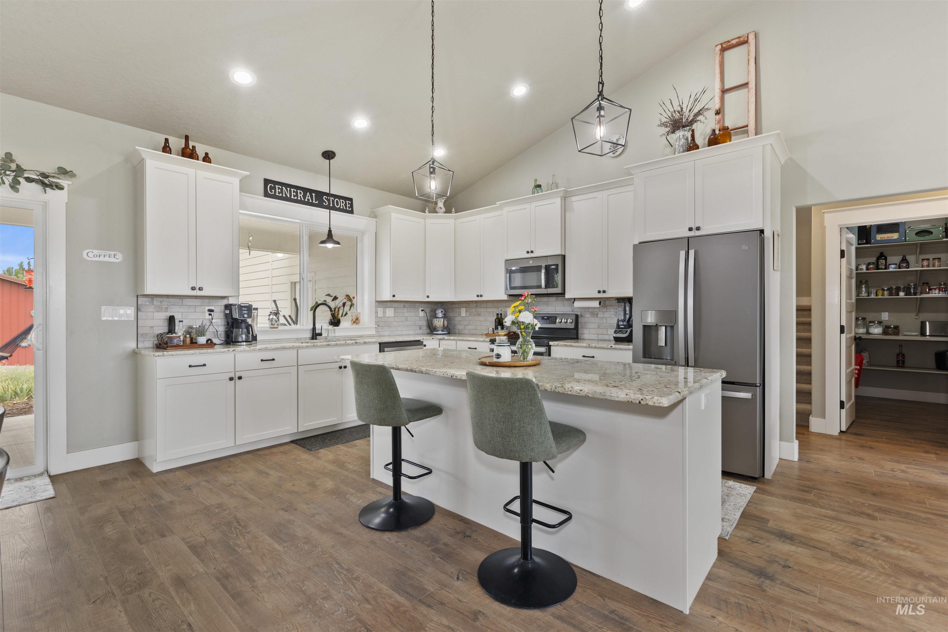 Kitchen with stainless steel appliances, a kitchen island, tasteful backsplash, white cabinets, and lofted ceiling