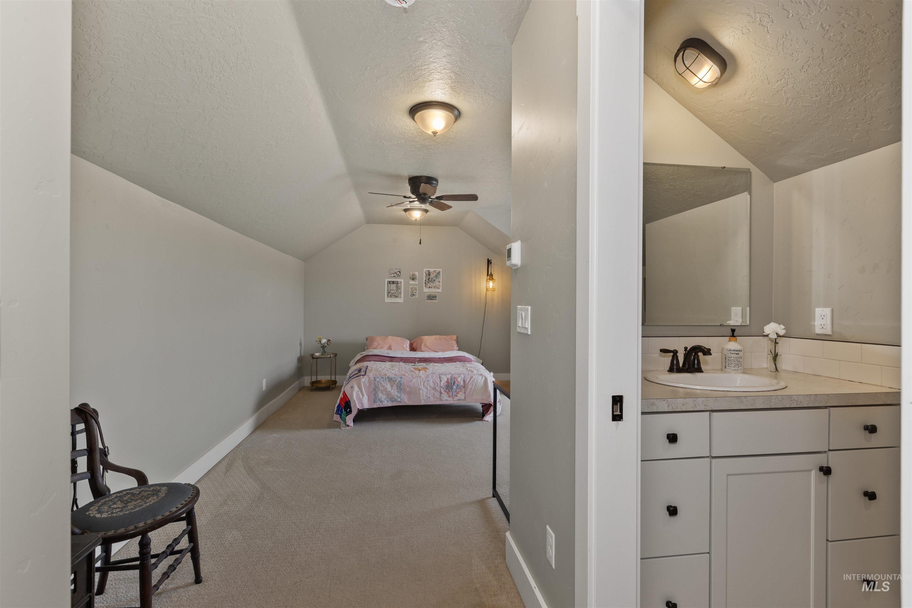 Bedroom with a textured ceiling, vaulted ceiling, and light colored carpet