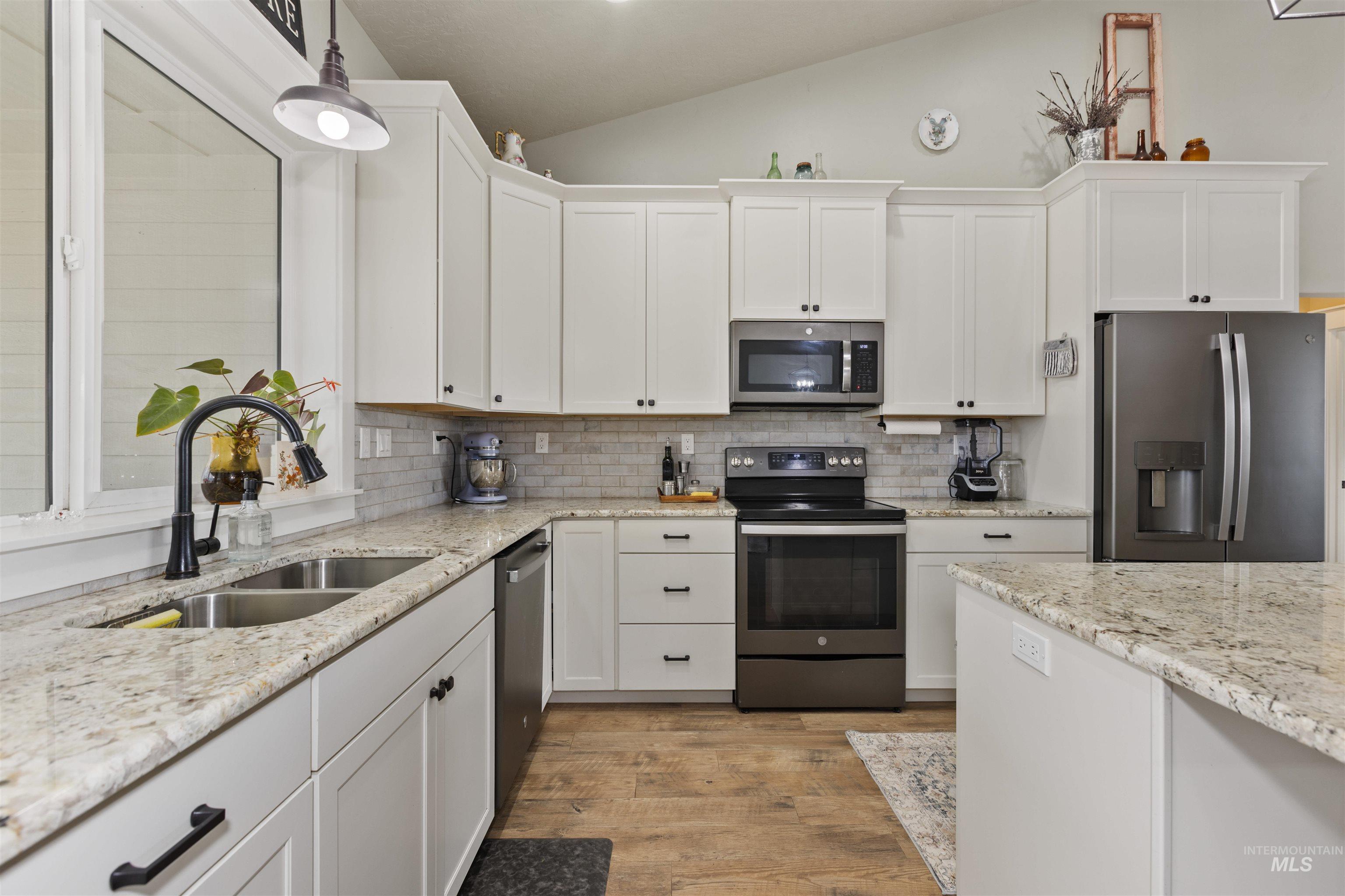 Kitchen featuring lofted ceiling, stainless steel appliances, white cabinetry, light wood-style flooring, and pendant lighting