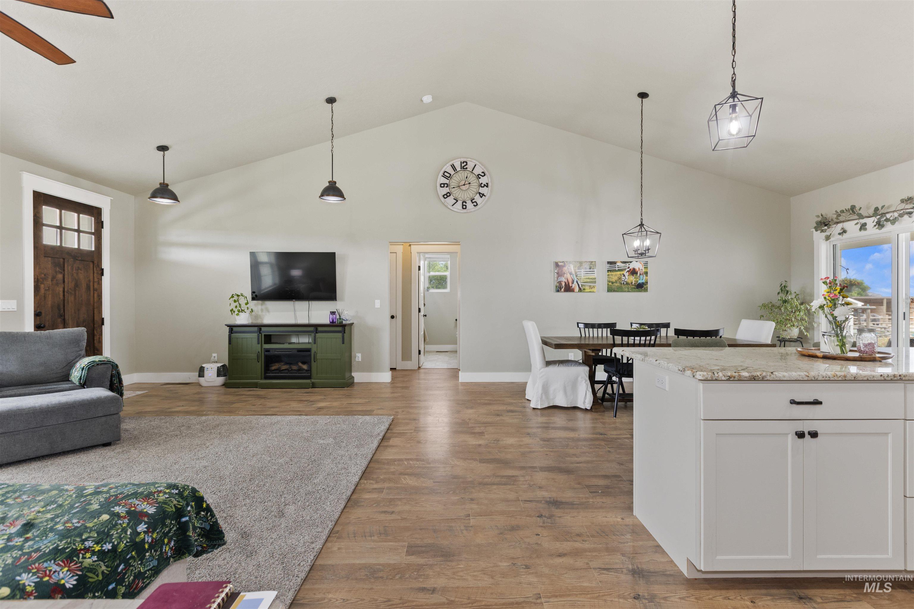 Living area featuring wood finished floors, ceiling fan, a glass covered fireplace, and high vaulted ceiling