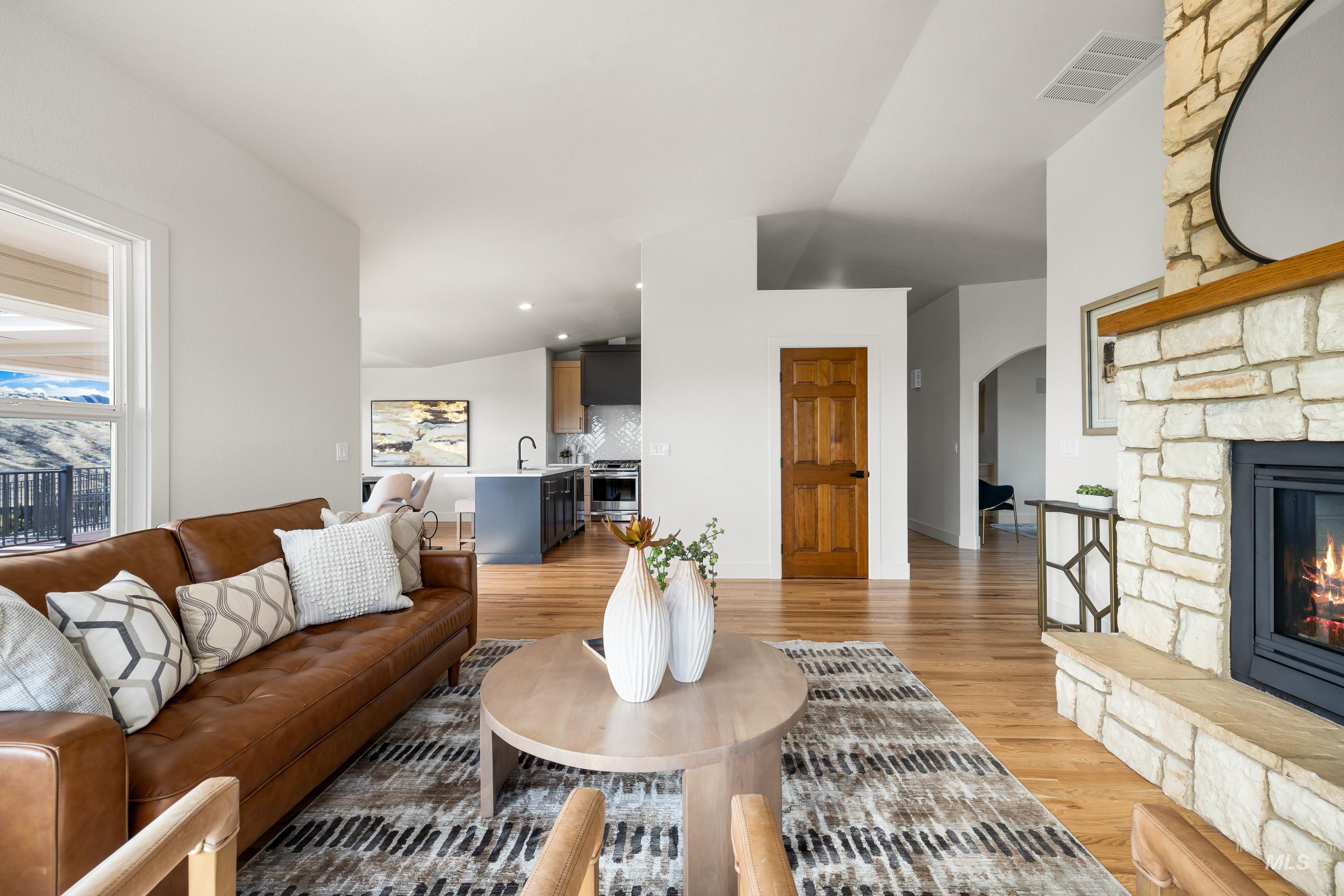 Living area featuring light wood-type flooring, vaulted ceiling, a stone fireplace, and arched walkways