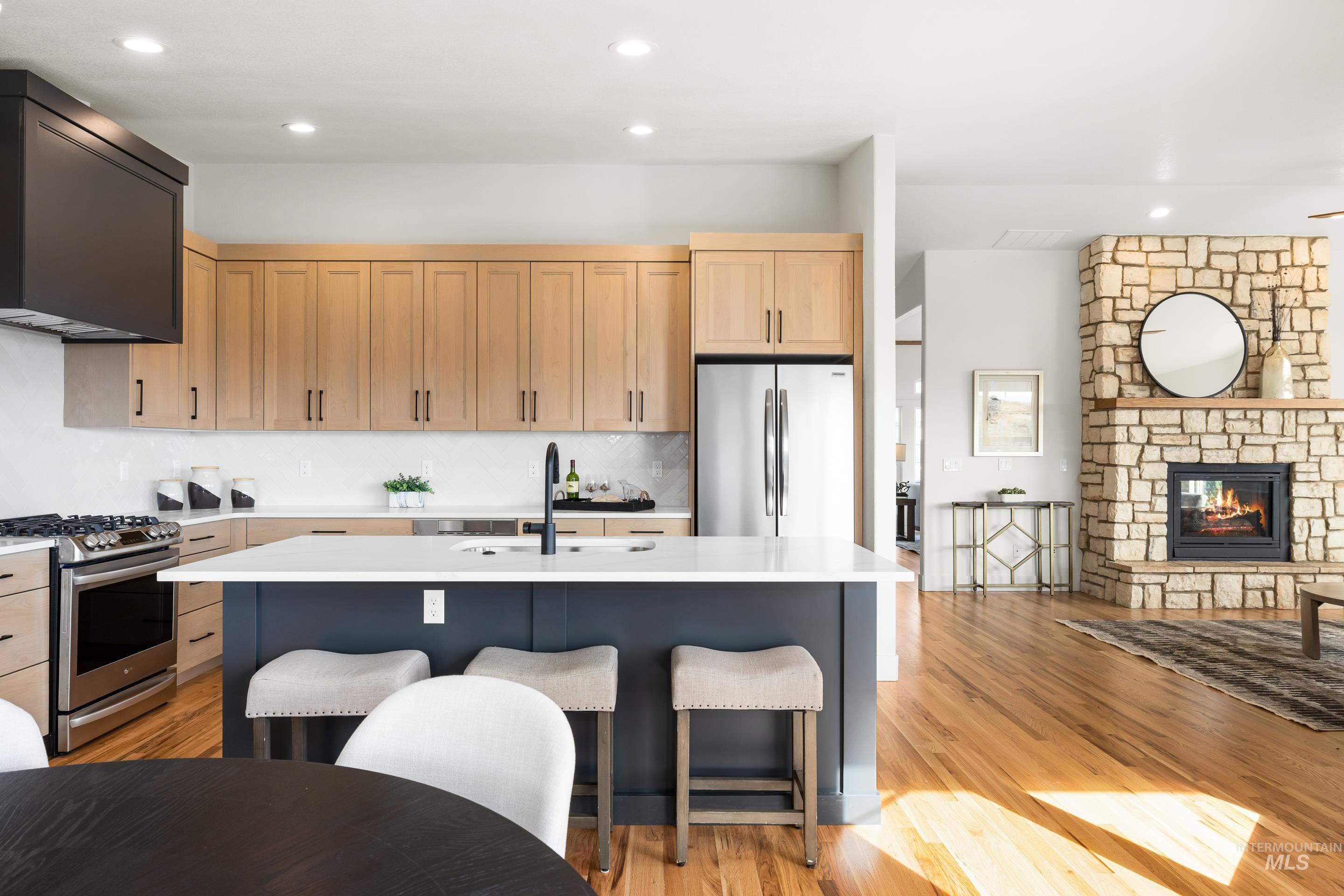 Kitchen featuring stainless steel appliances, light brown cabinetry, ventilation hood, light wood-style flooring, and recessed lighting
