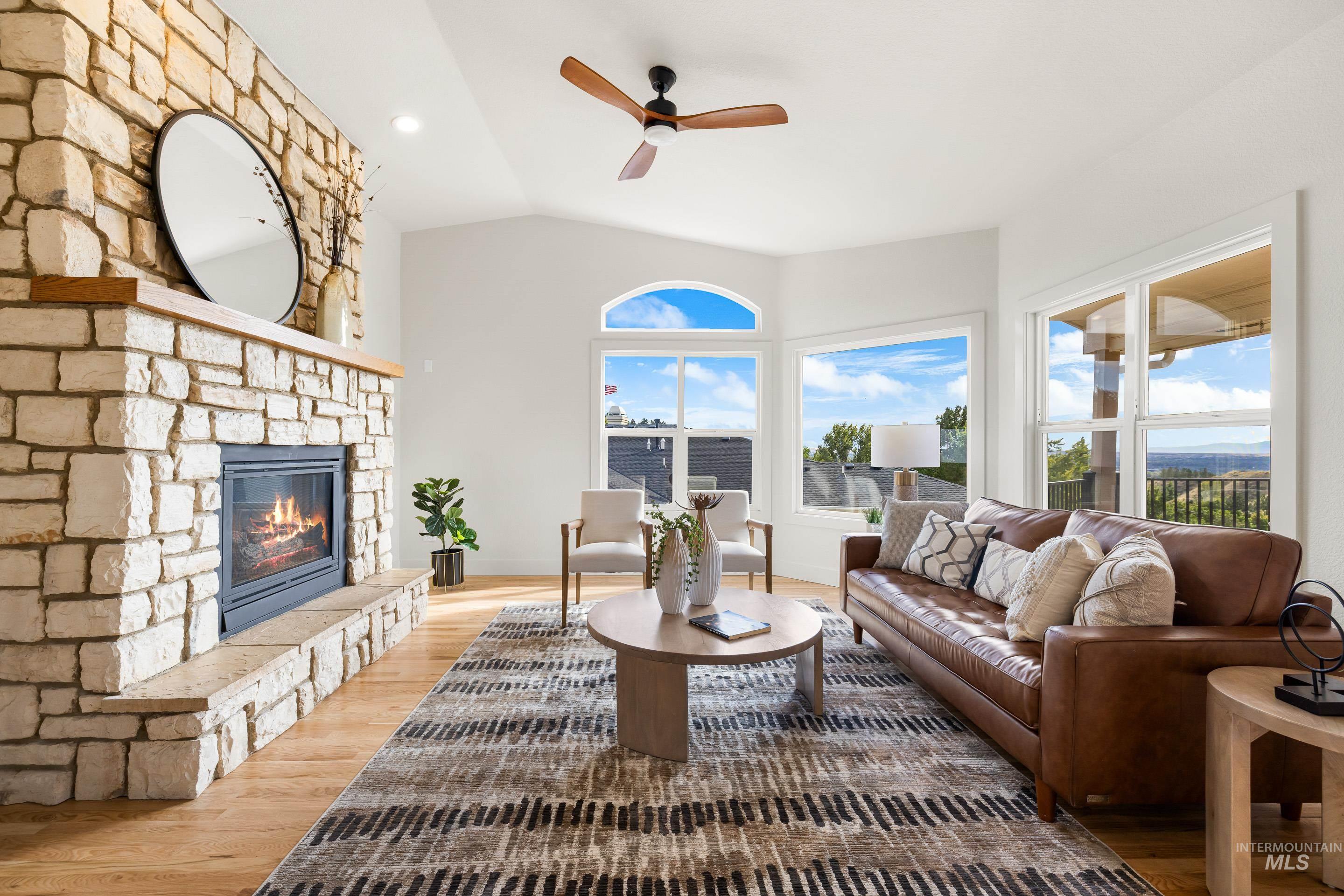 Living room featuring vaulted ceiling, wood finished floors, a ceiling fan, a stone fireplace, and recessed lighting