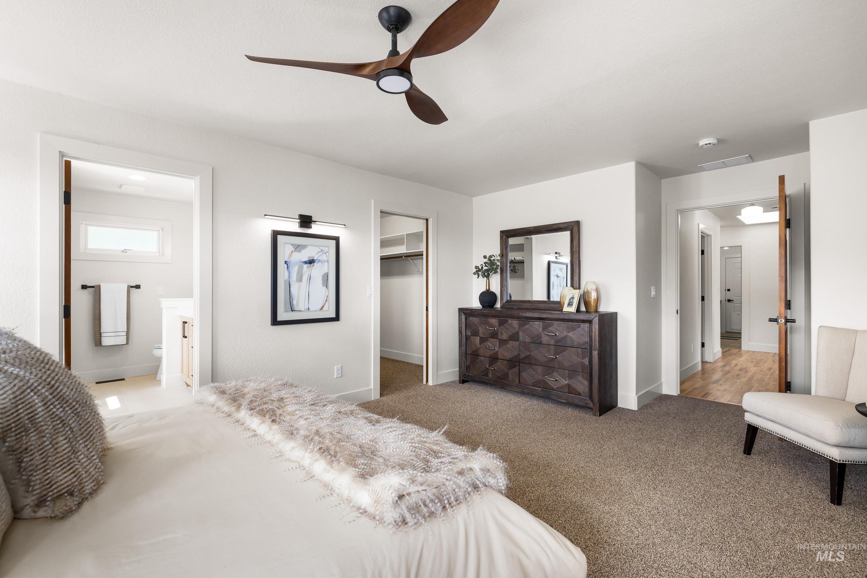 Bedroom with ensuite bathroom, a spacious closet, carpet flooring, and a ceiling fan
