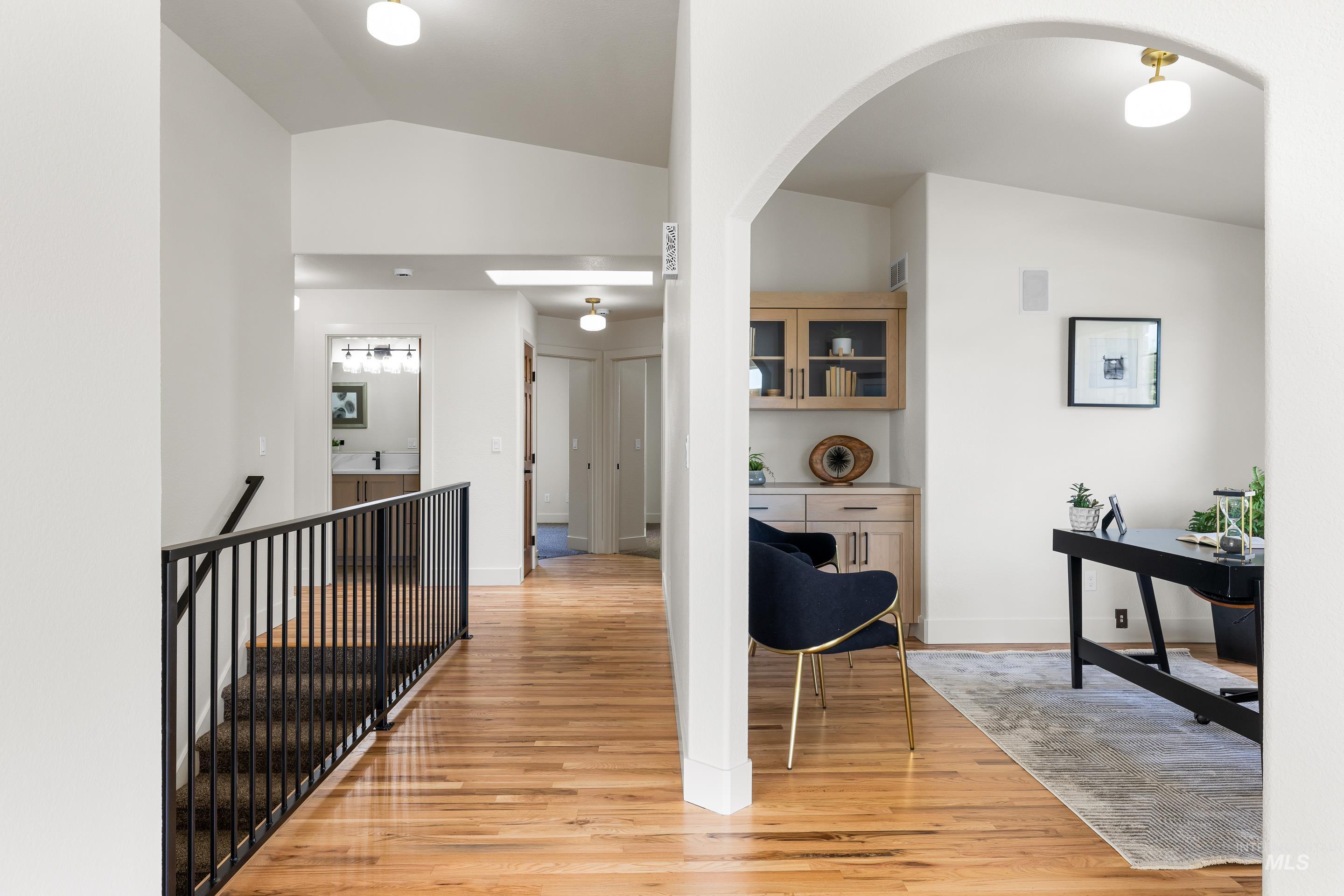 Hallway featuring an upstairs landing, light wood-style floors, vaulted ceiling, and arched walkways