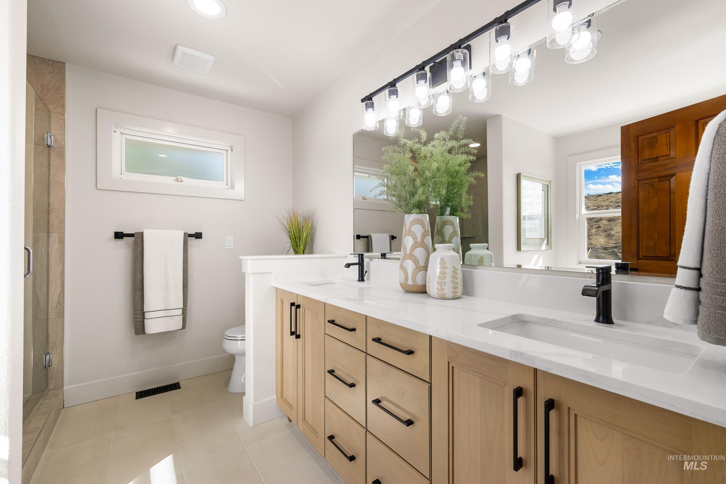 Full bath featuring a shower stall, double vanity, and light tile patterned floors