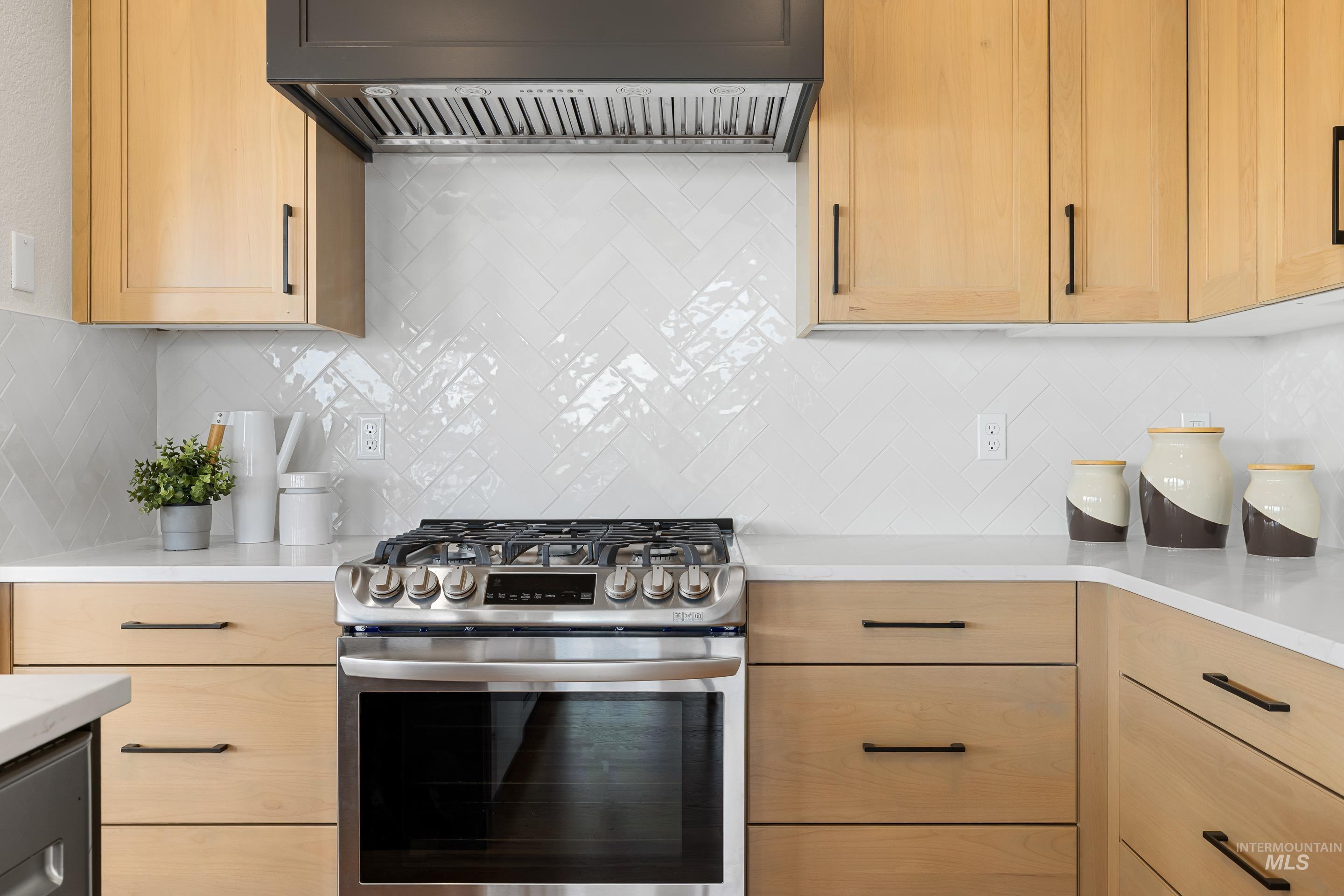 Kitchen featuring stainless steel gas range oven, light brown cabinetry, and decorative backsplash