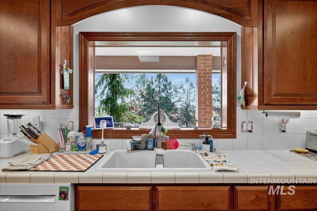 Kitchen with brown cabinetry, tasteful backsplash, and tile counters