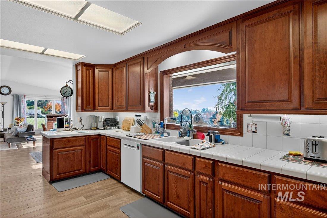 Kitchen with brown cabinetry, tile counters, decorative backsplash, and light wood finished floors