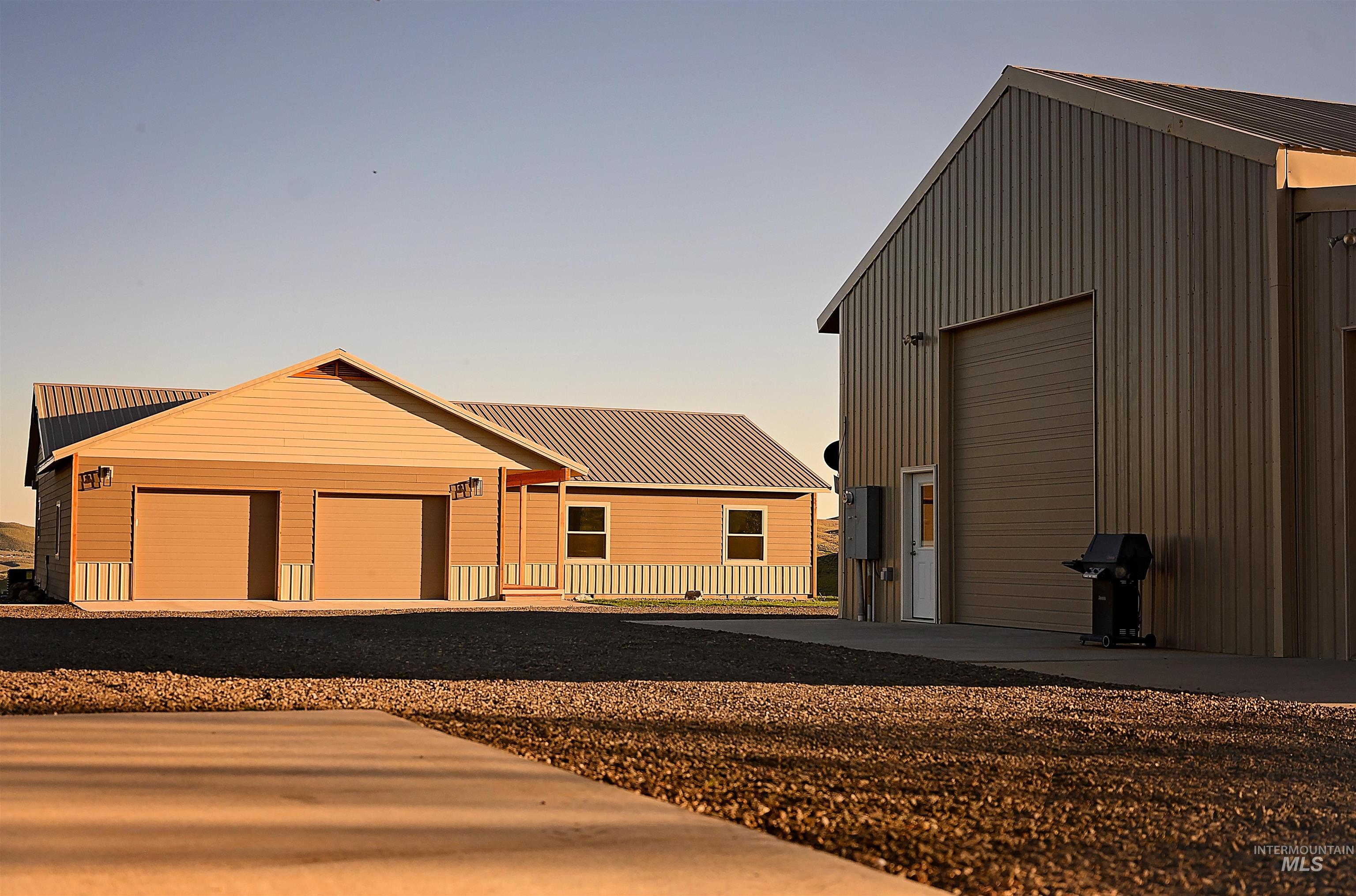 View of front of property featuring an attached garage, an outbuilding, and gravel driveway