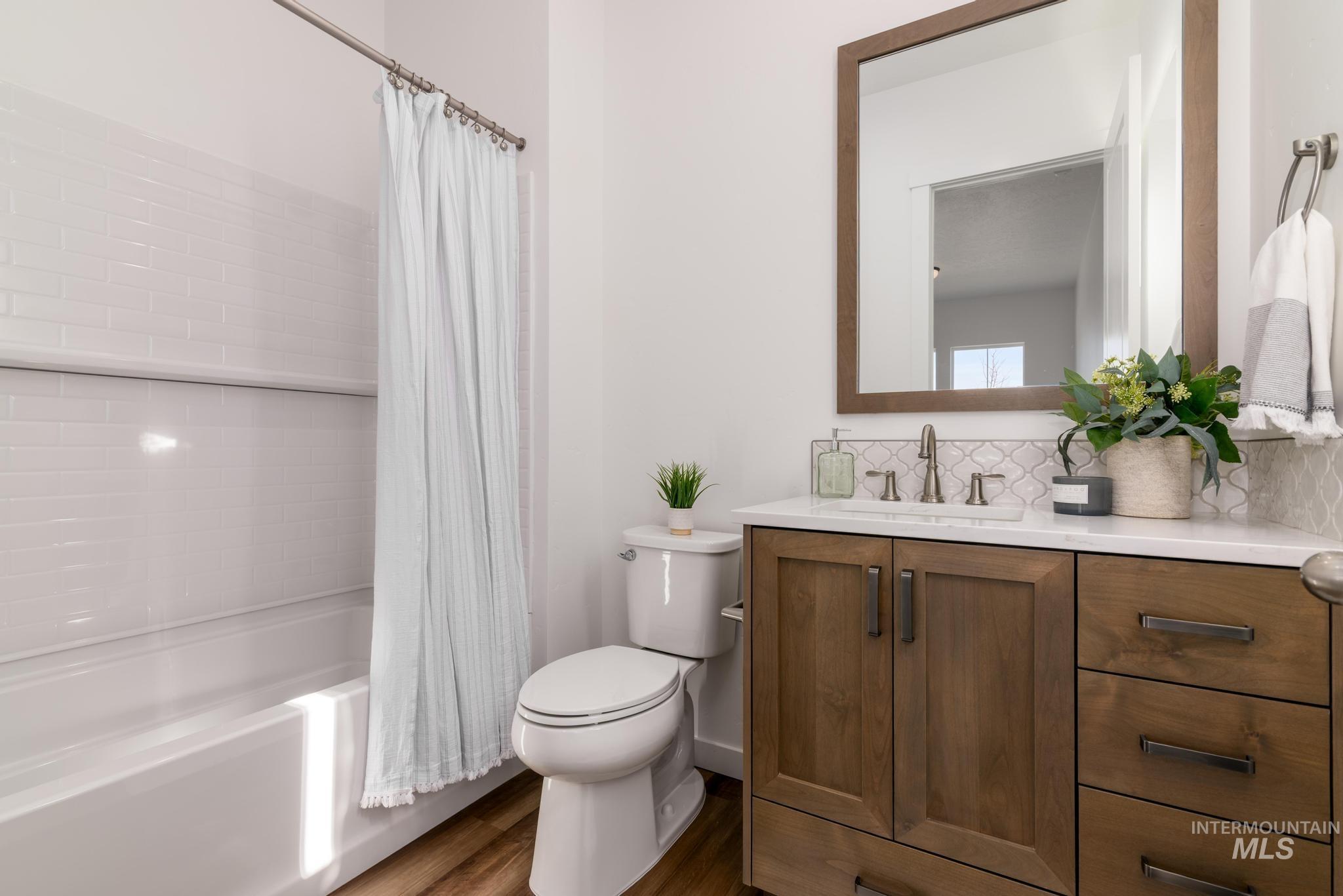 Bathroom with vanity, shower / bath combo with shower curtain, decorative backsplash, and dark wood finished floors