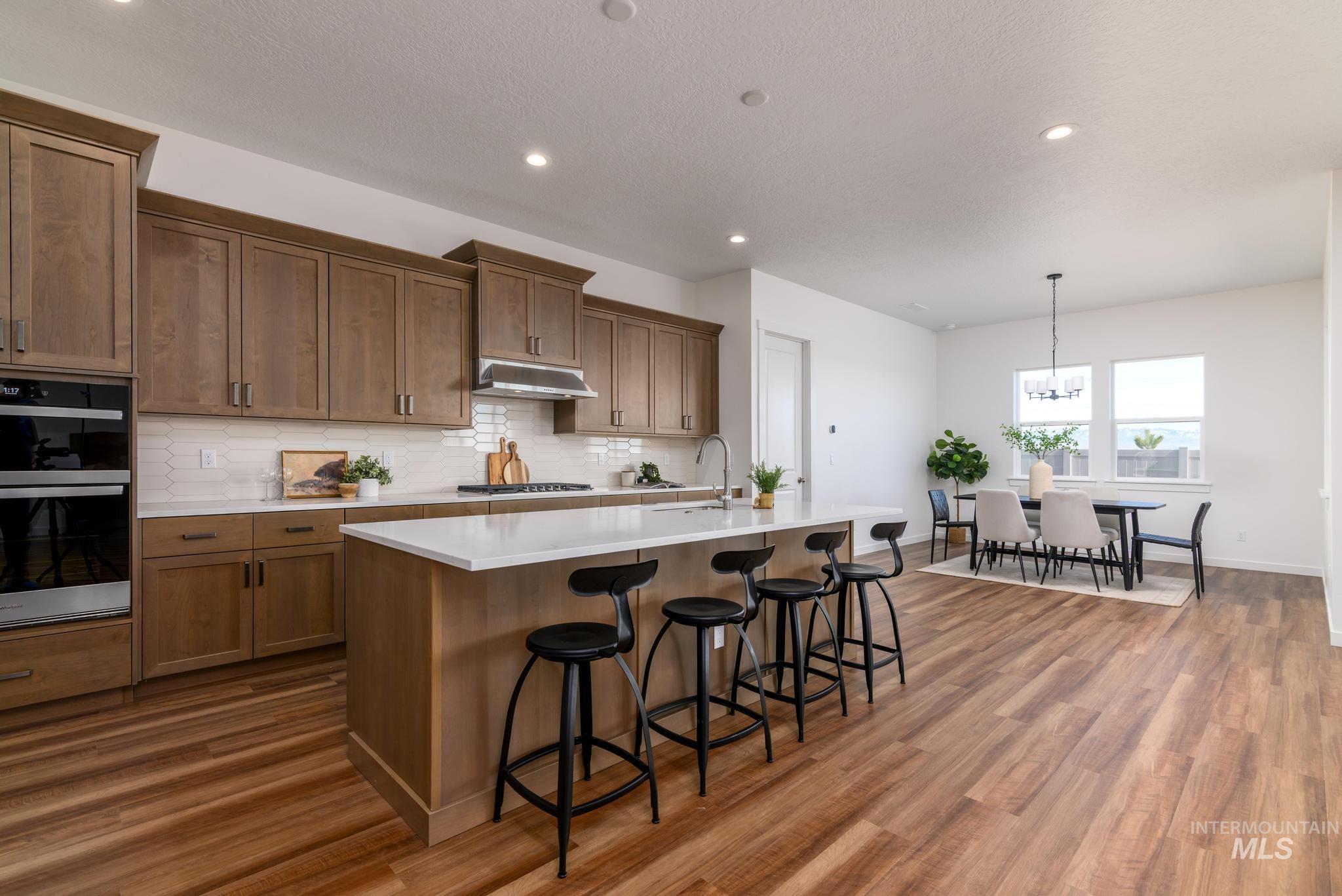 Kitchen with backsplash, double oven, brown cabinetry, pendant lighting, and recessed lighting