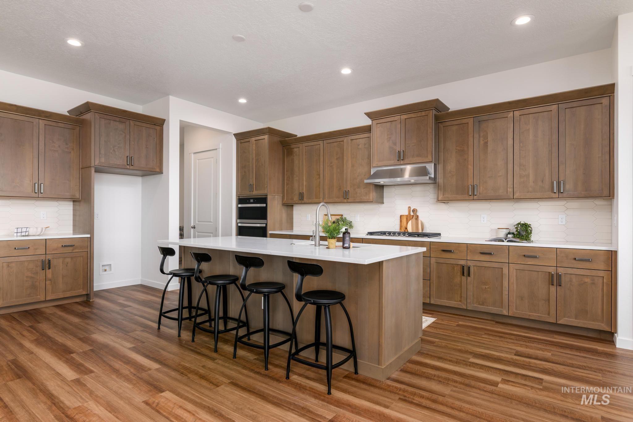 Kitchen featuring backsplash, a kitchen bar, recessed lighting, a kitchen island with sink, and dark wood-type flooring