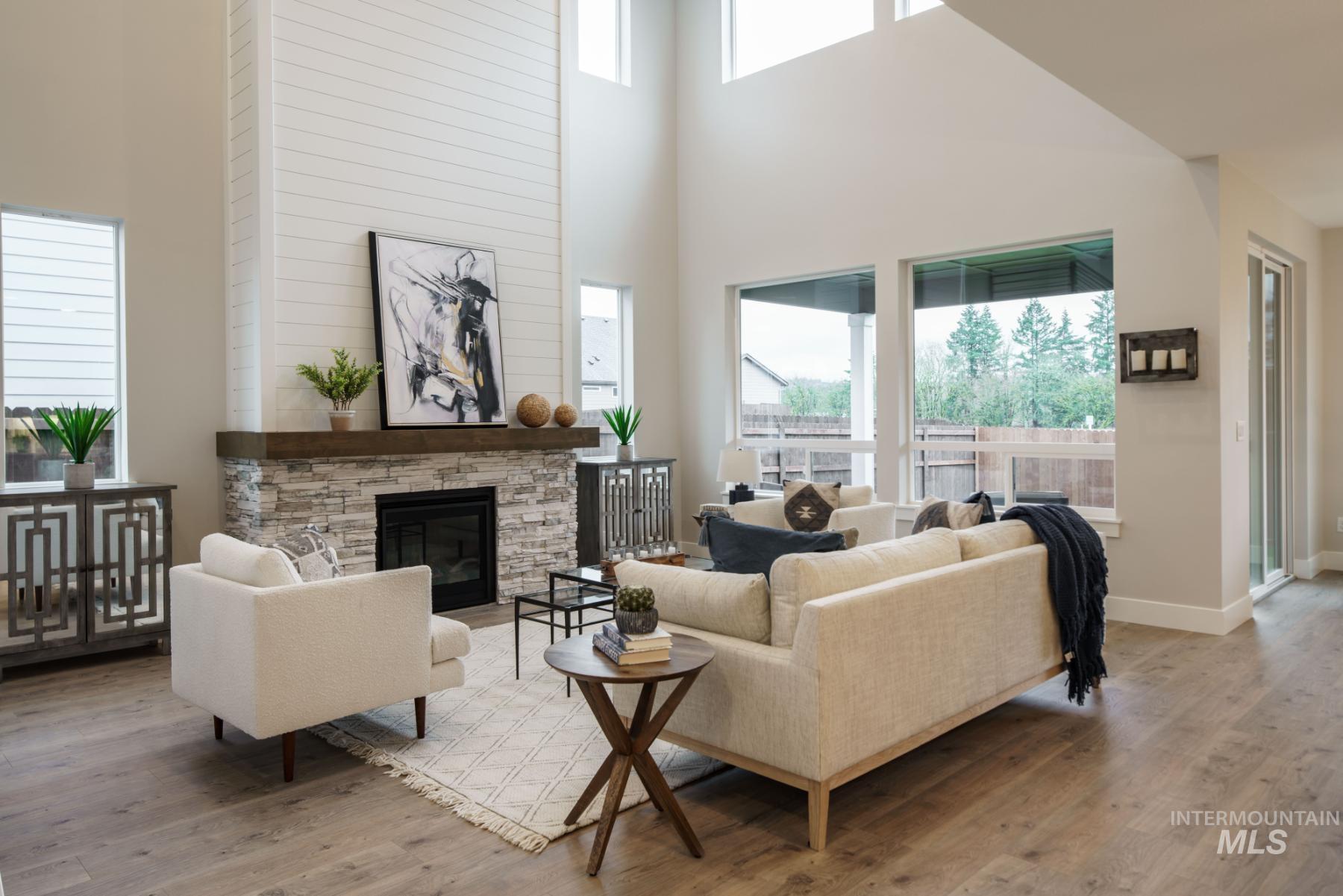 Living room featuring a stone fireplace, wood finished floors, and a towering ceiling