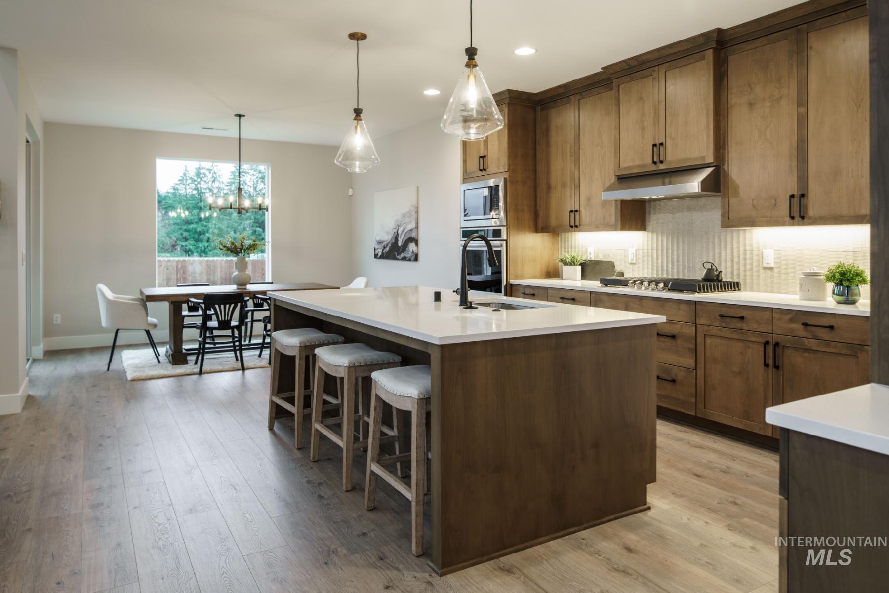 Kitchen with backsplash, light countertops, light wood-style floors, a kitchen island with sink, and ventilation hood