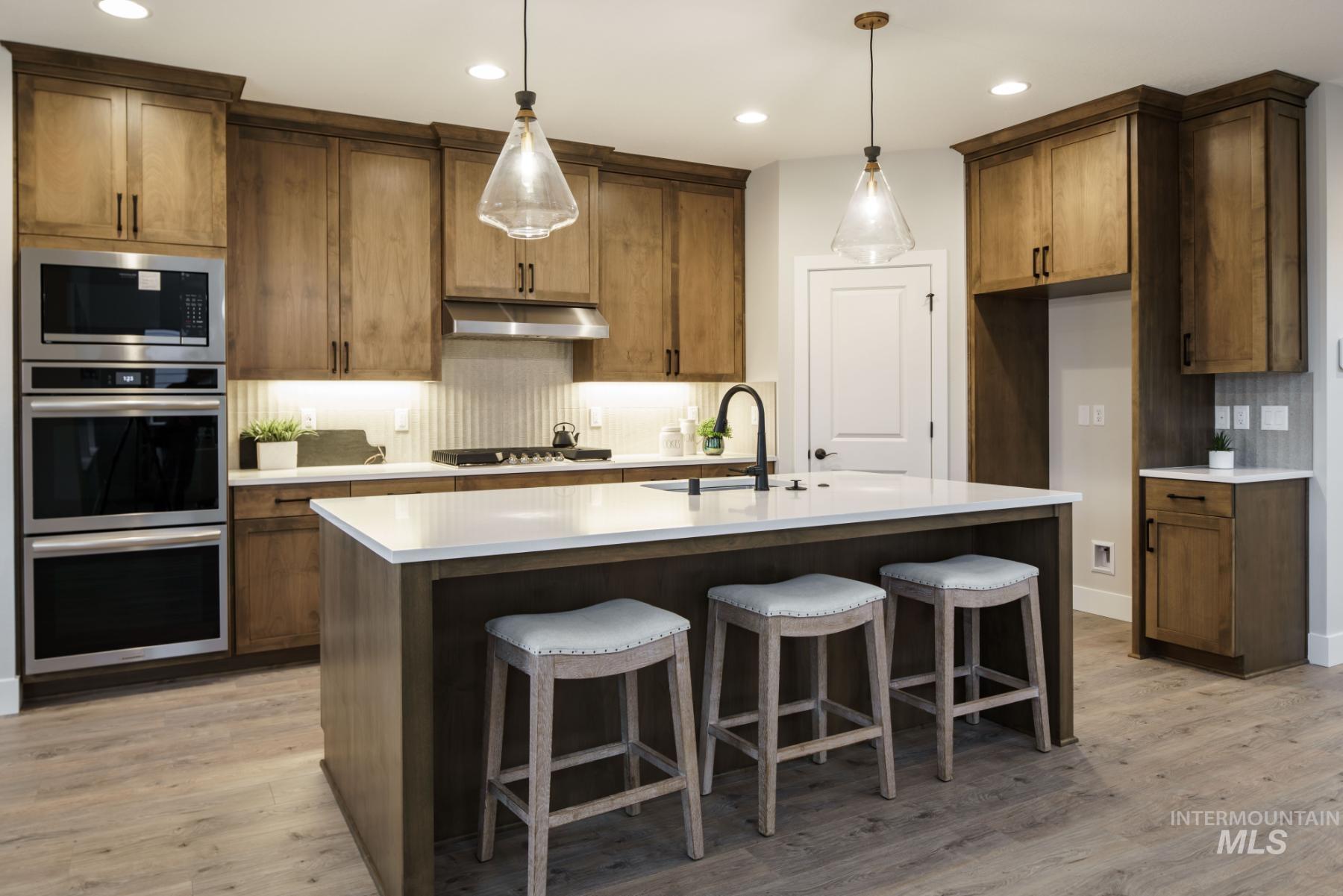 Kitchen with backsplash, appliances with stainless steel finishes, recessed lighting, light wood-type flooring, and an island with sink