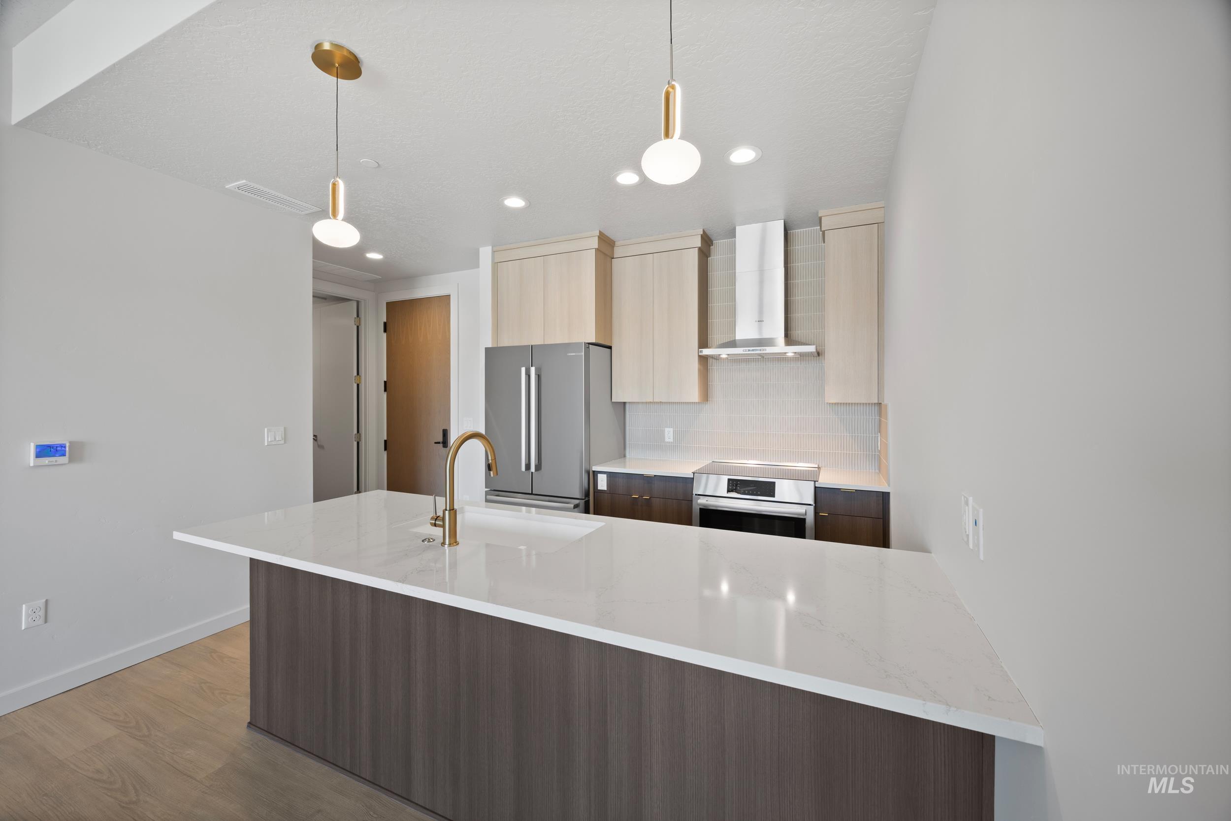 Kitchen with tasteful backsplash, modern cabinets, wall chimney range hood, light stone counters, and light wood finished floors