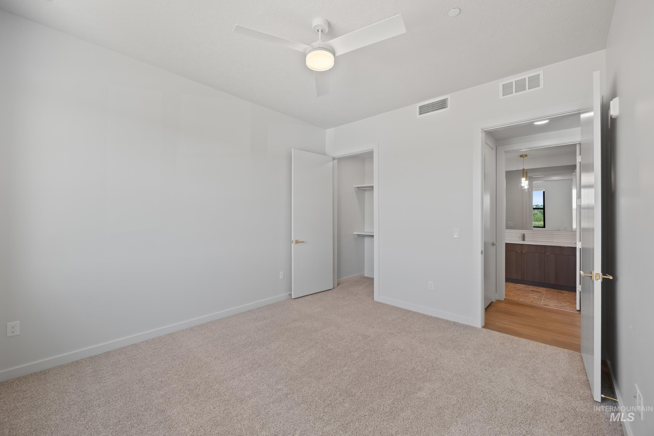 Unfurnished bedroom with a spacious closet, light colored carpet, and a ceiling fan