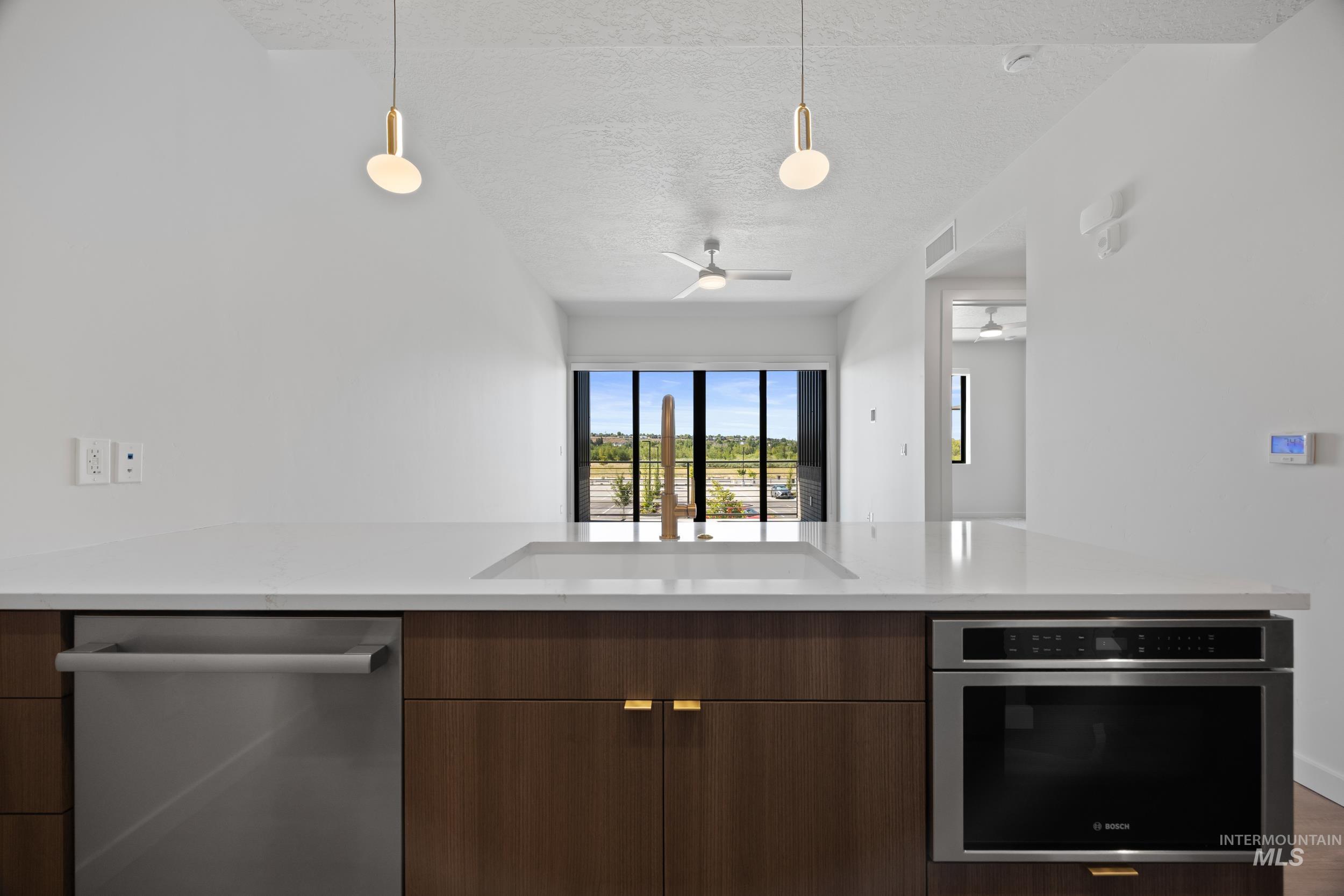 Kitchen with stainless steel appliances, modern cabinets, a textured ceiling, decorative light fixtures, and light stone counters