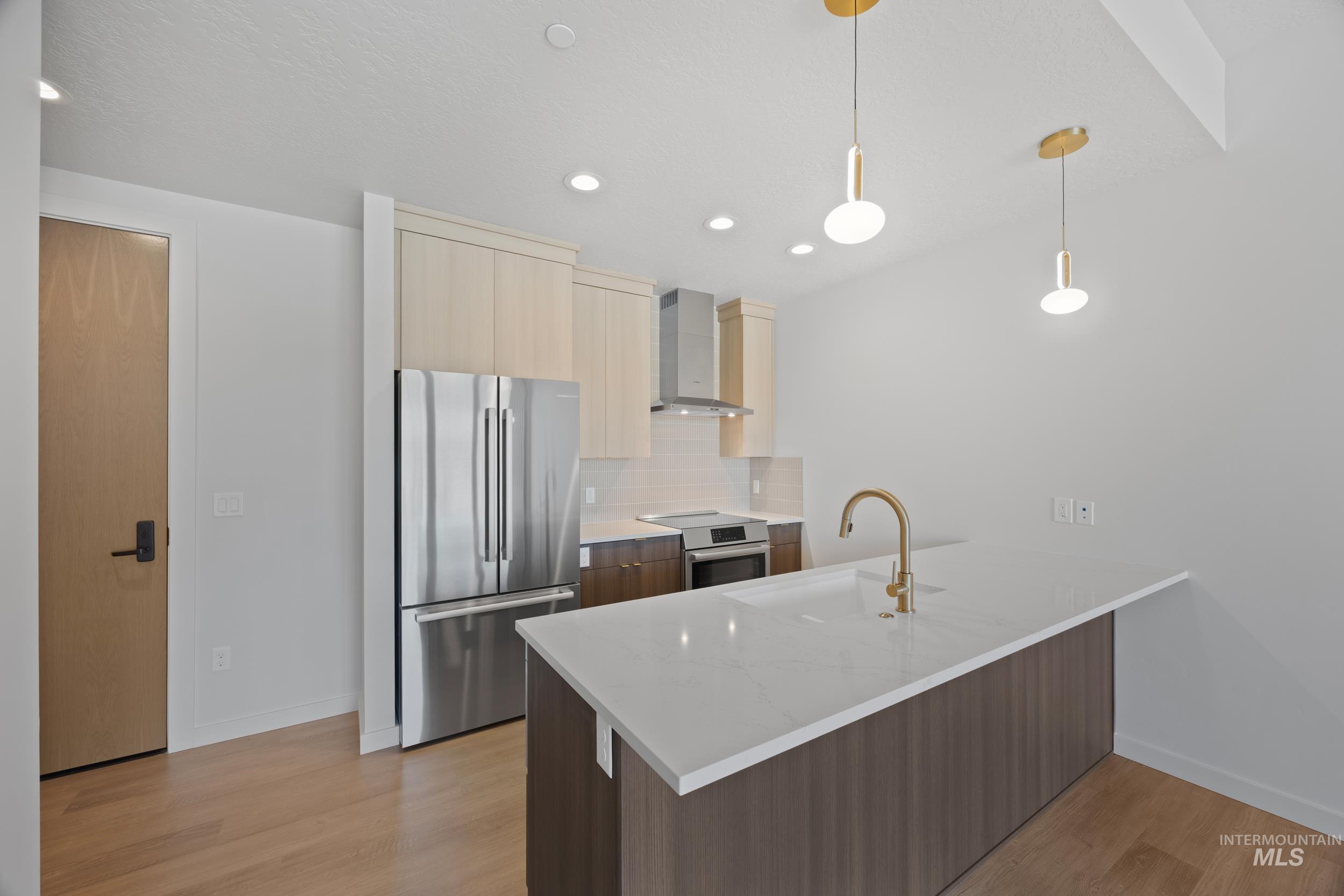 Kitchen featuring modern cabinets, stainless steel appliances, light stone countertops, decorative backsplash, and decorative light fixtures