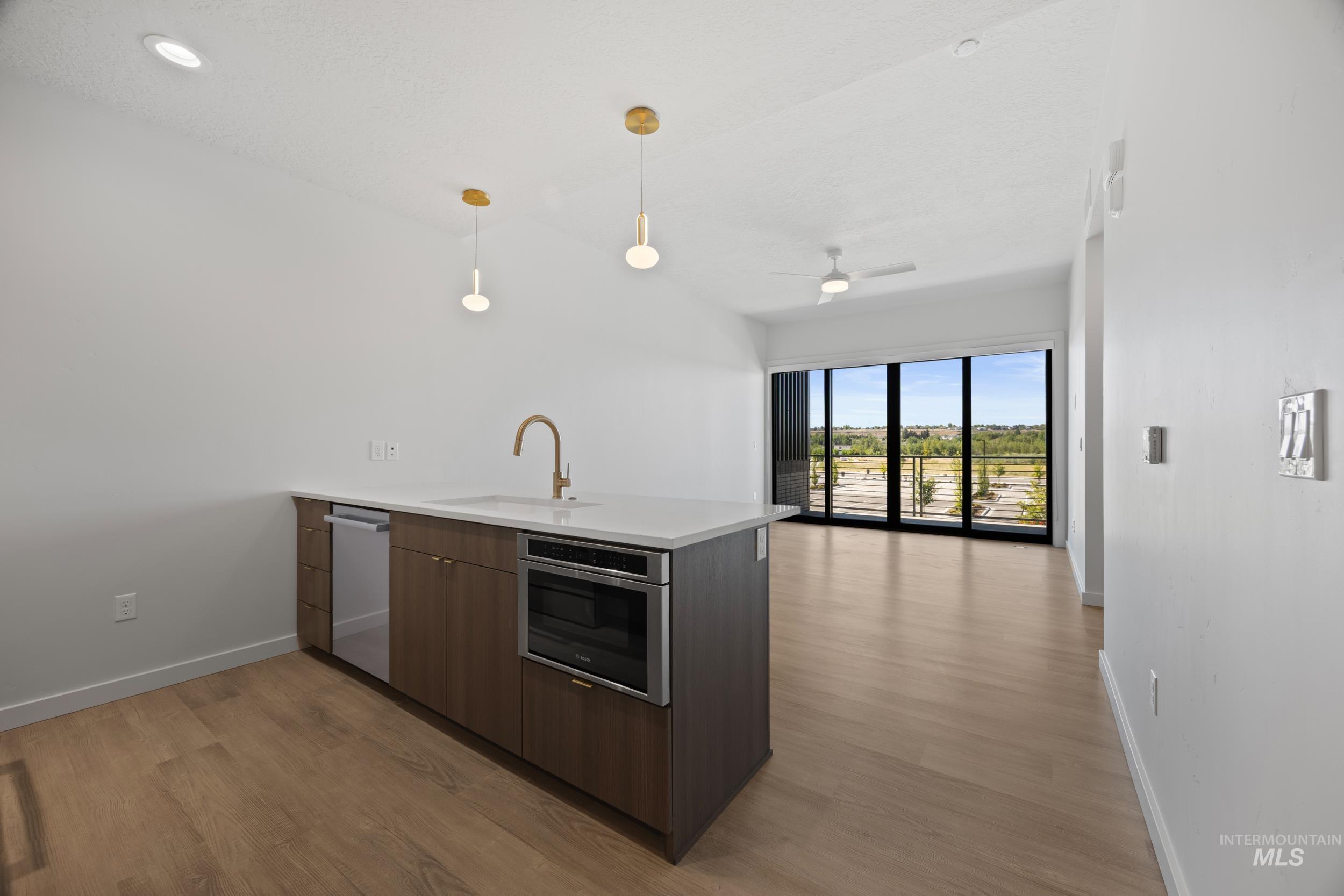 Kitchen with a peninsula, hanging light fixtures, modern cabinets, light wood-style flooring, and appliances with stainless steel finishes