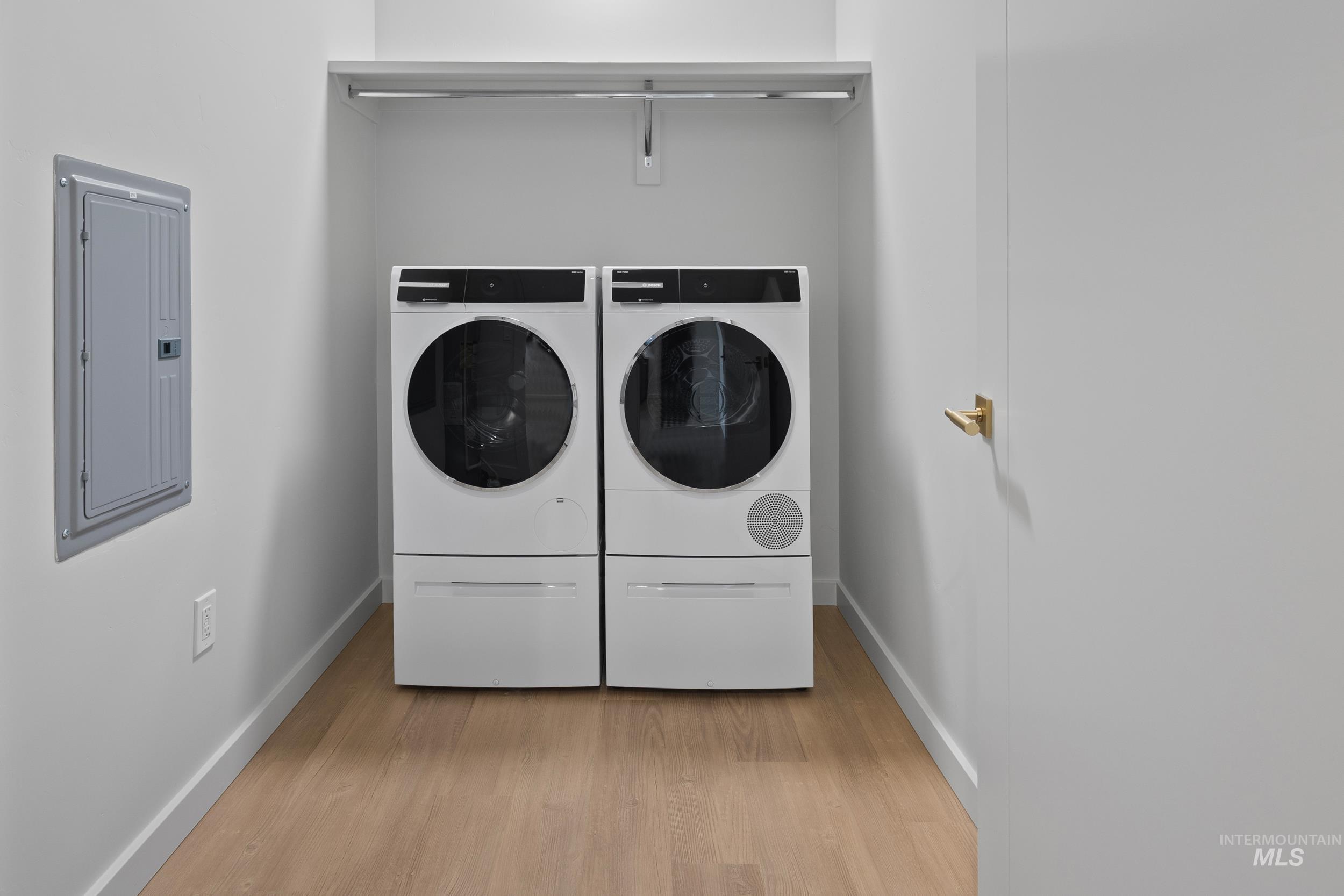 Washroom with light wood-style flooring, electric panel, and separate washer and dryer