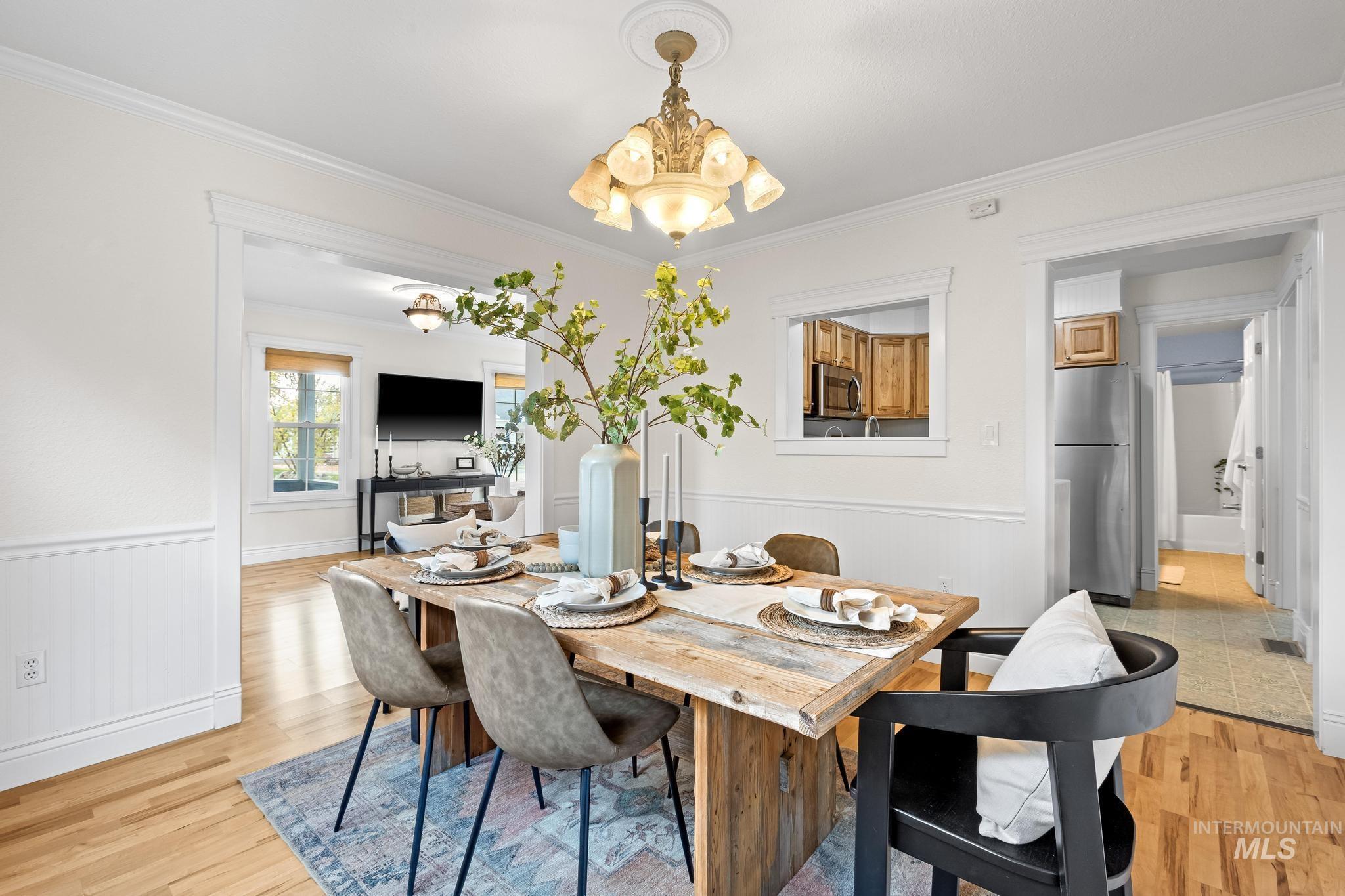 Dining space featuring a wainscoted wall, crown molding, light wood-style floors, and a chandelier