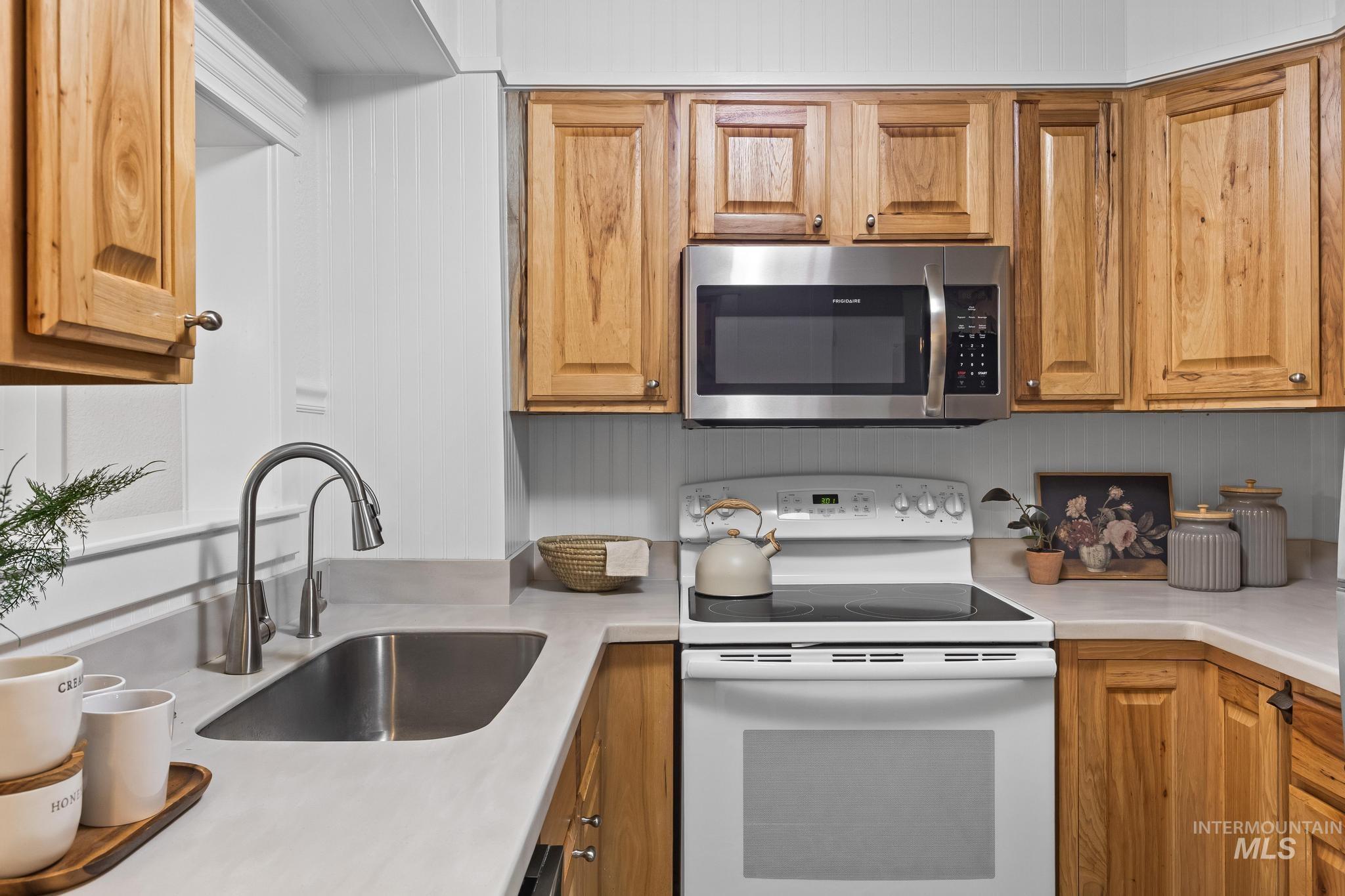 Kitchen featuring white electric stove, light countertops, stainless steel microwave, and brown cabinetry