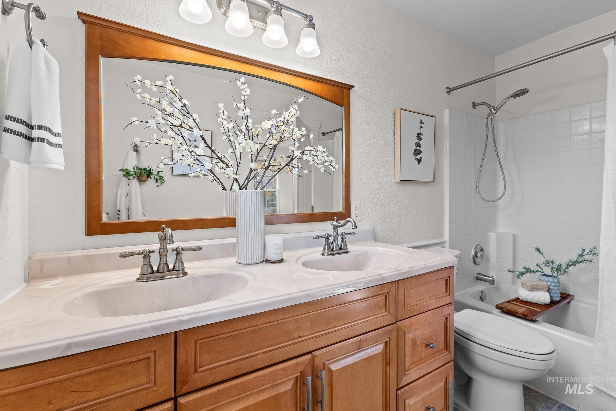 Bathroom with shower / bathtub combination with curtain, double vanity, and a textured wall