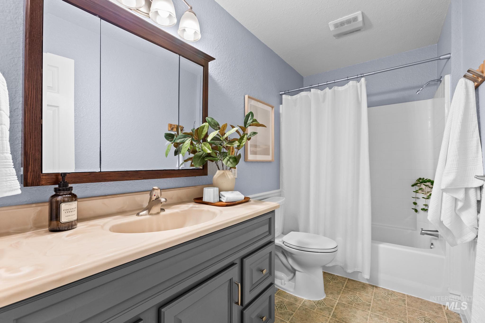 Full bath featuring shower / bath combo with shower curtain, vanity, and a textured wall