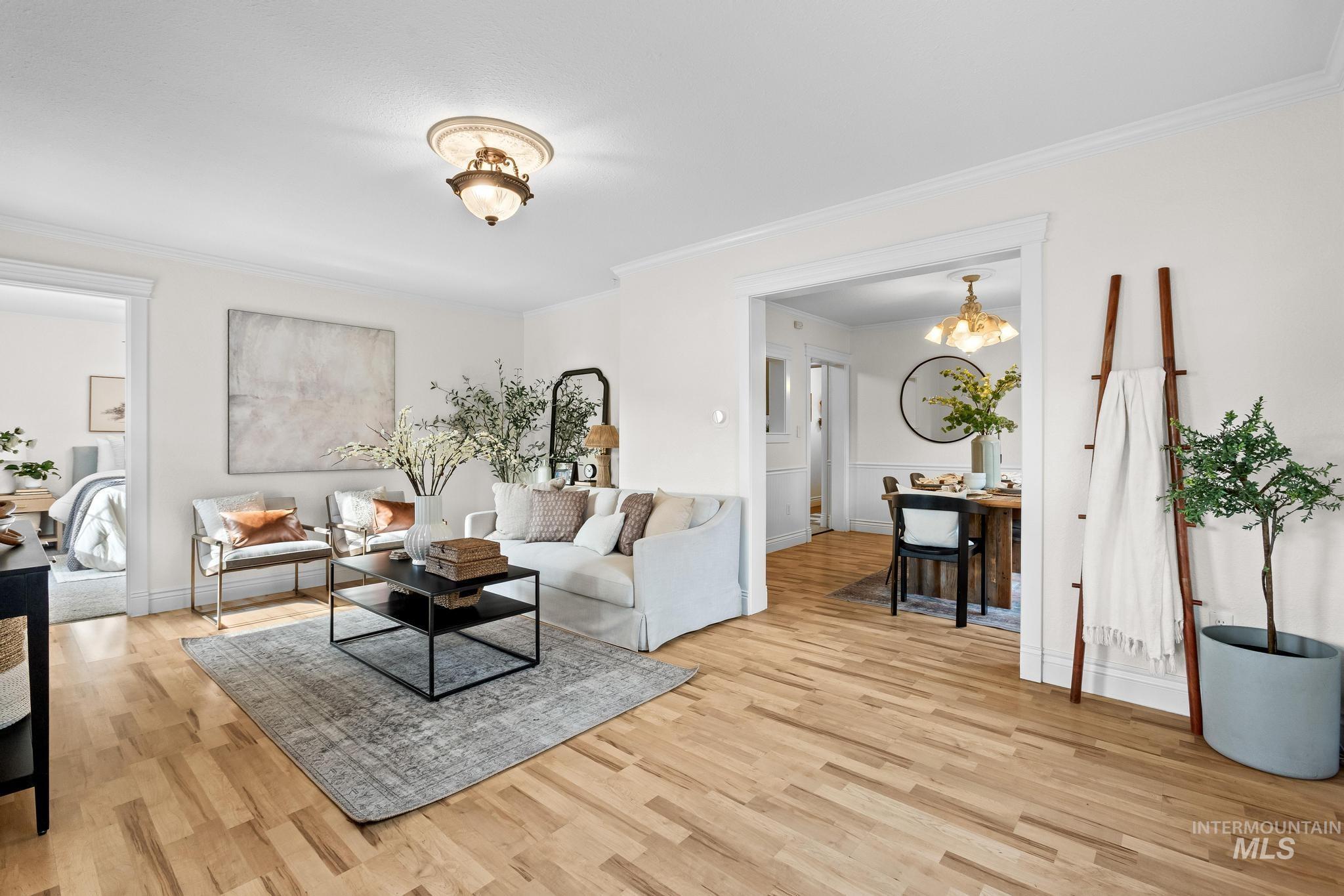 Living area featuring ornamental molding, light wood-style floors, and a chandelier