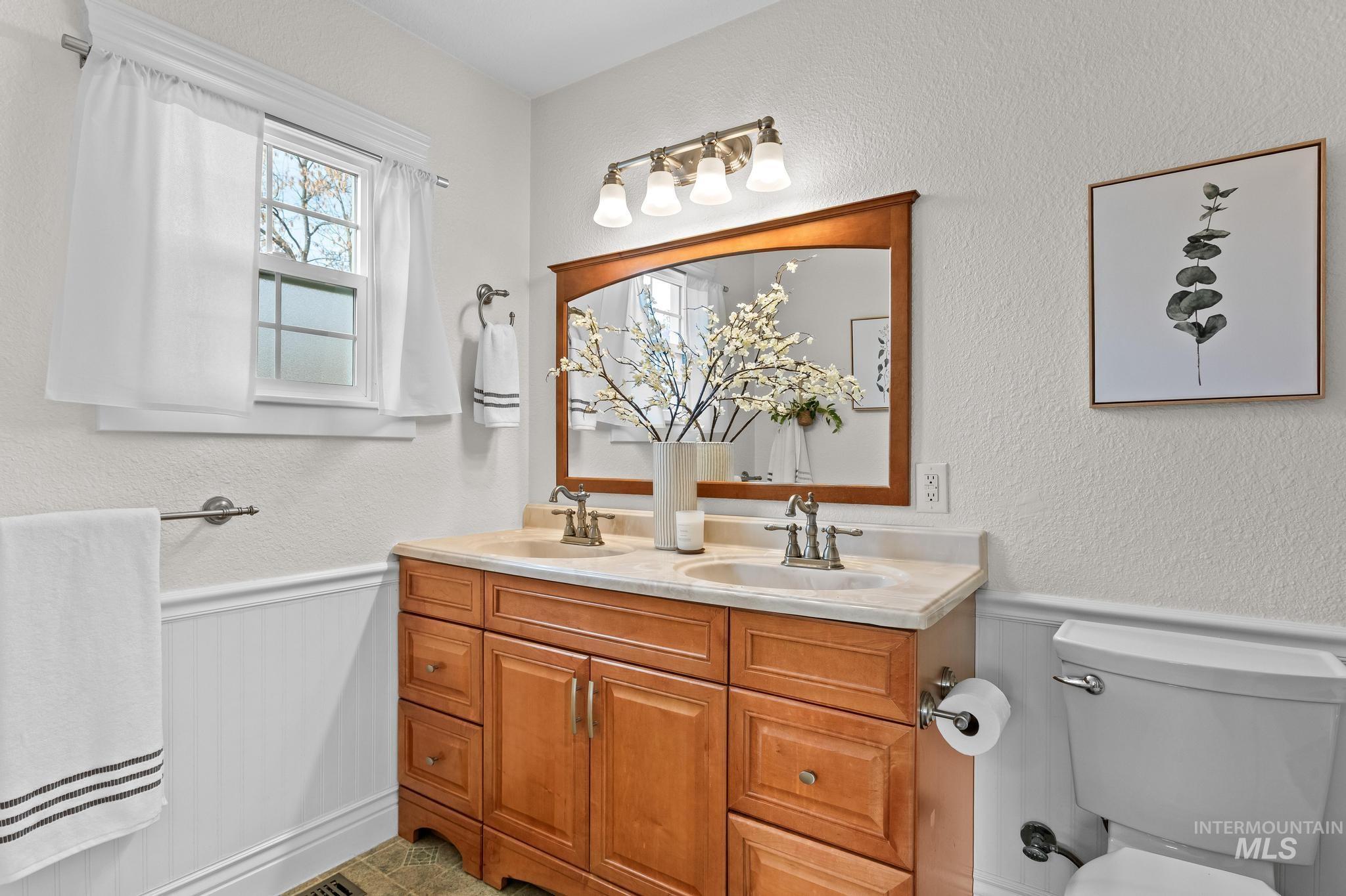 Full bathroom with a textured wall, wainscoting, and double vanity
