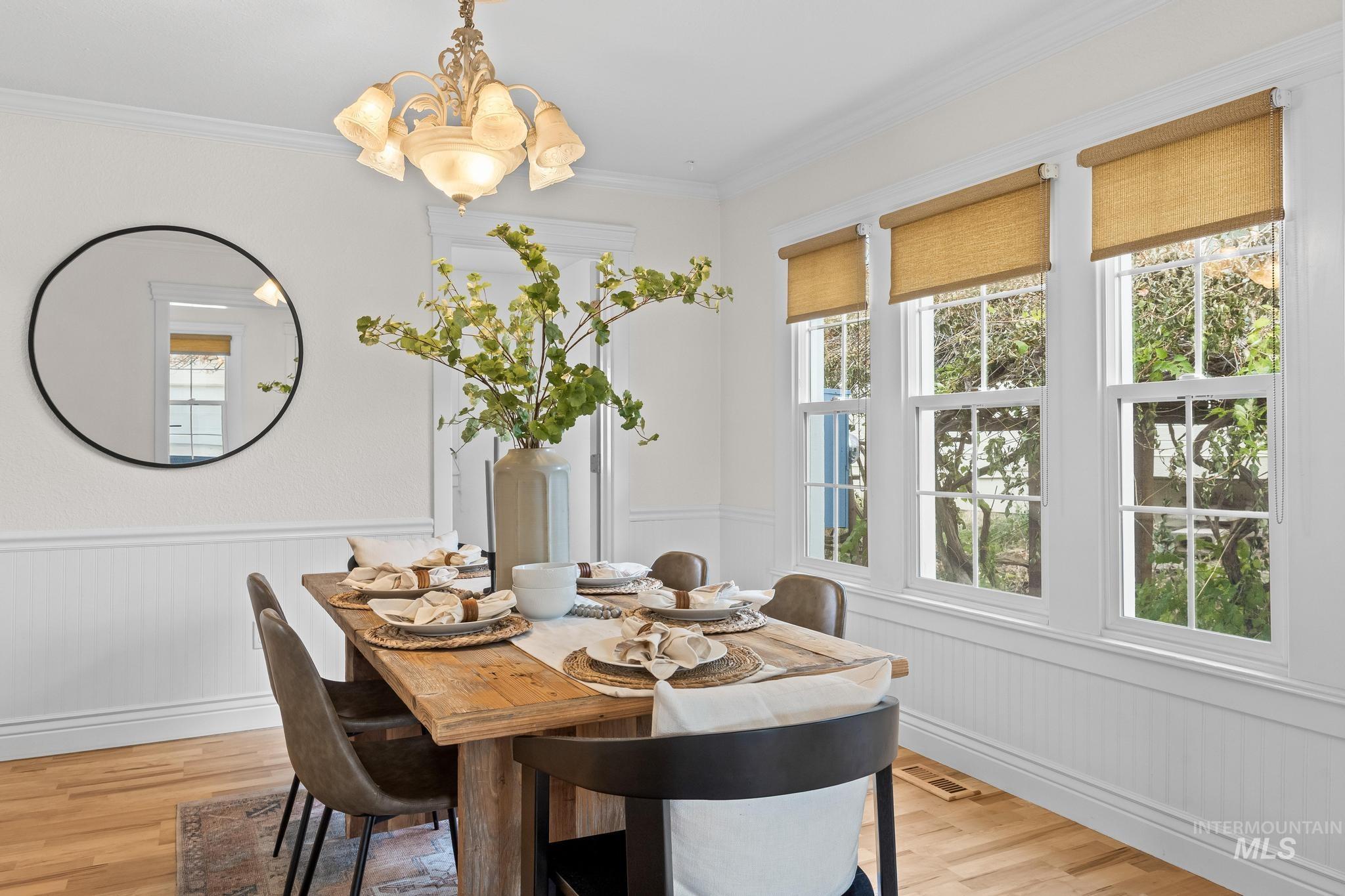 Dining room featuring wainscoting, light wood-type flooring, crown molding, and a chandelier