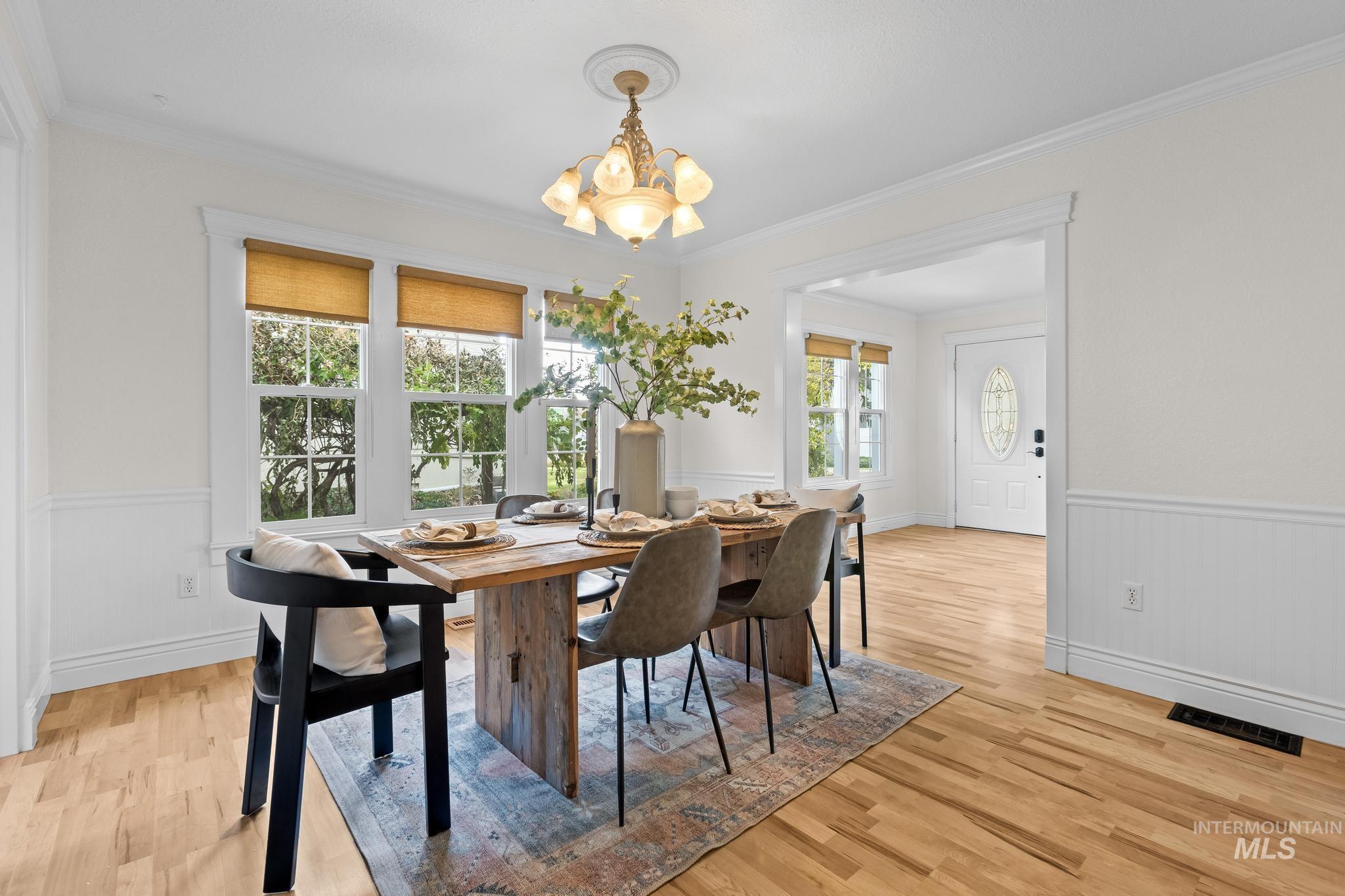 Dining area featuring a wainscoted wall, light wood-type flooring, ornamental molding, and a chandelier